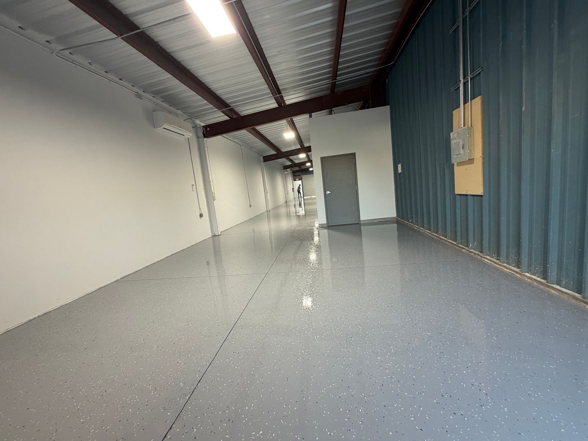Empty warehouse interior with white walls, blue side panel, and glossy speckled floor