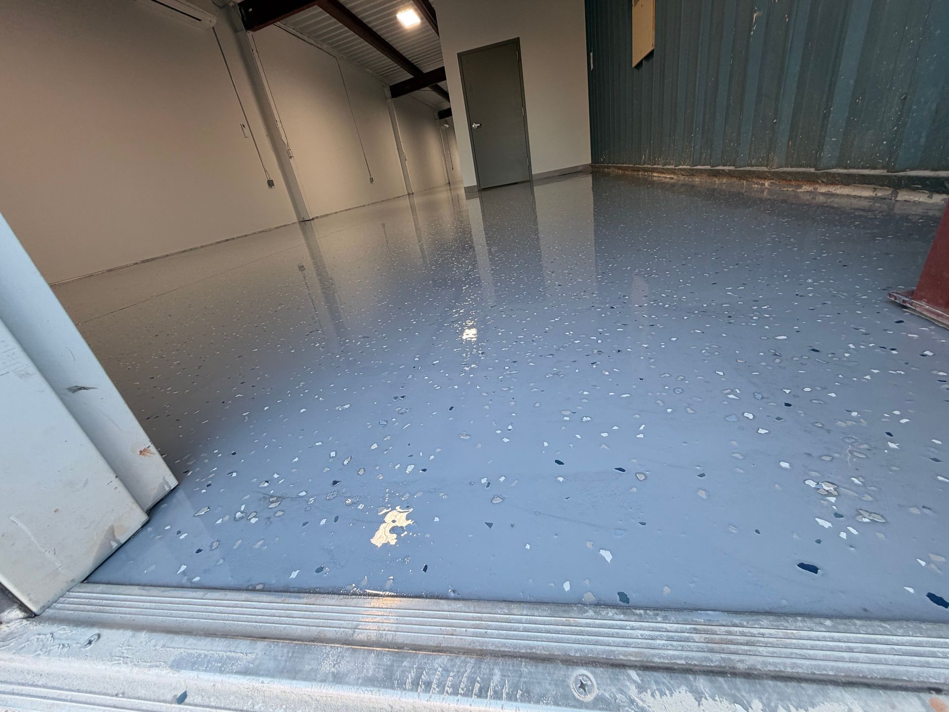 Empty industrial room with glossy blue floor, white speckles, and a doorway opening inside