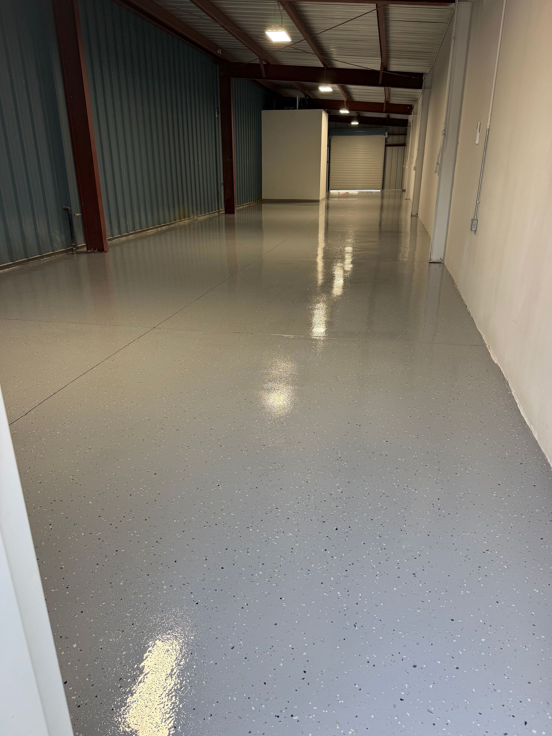 Empty warehouse aisle with glossy speckled epoxy floor and metal storage walls