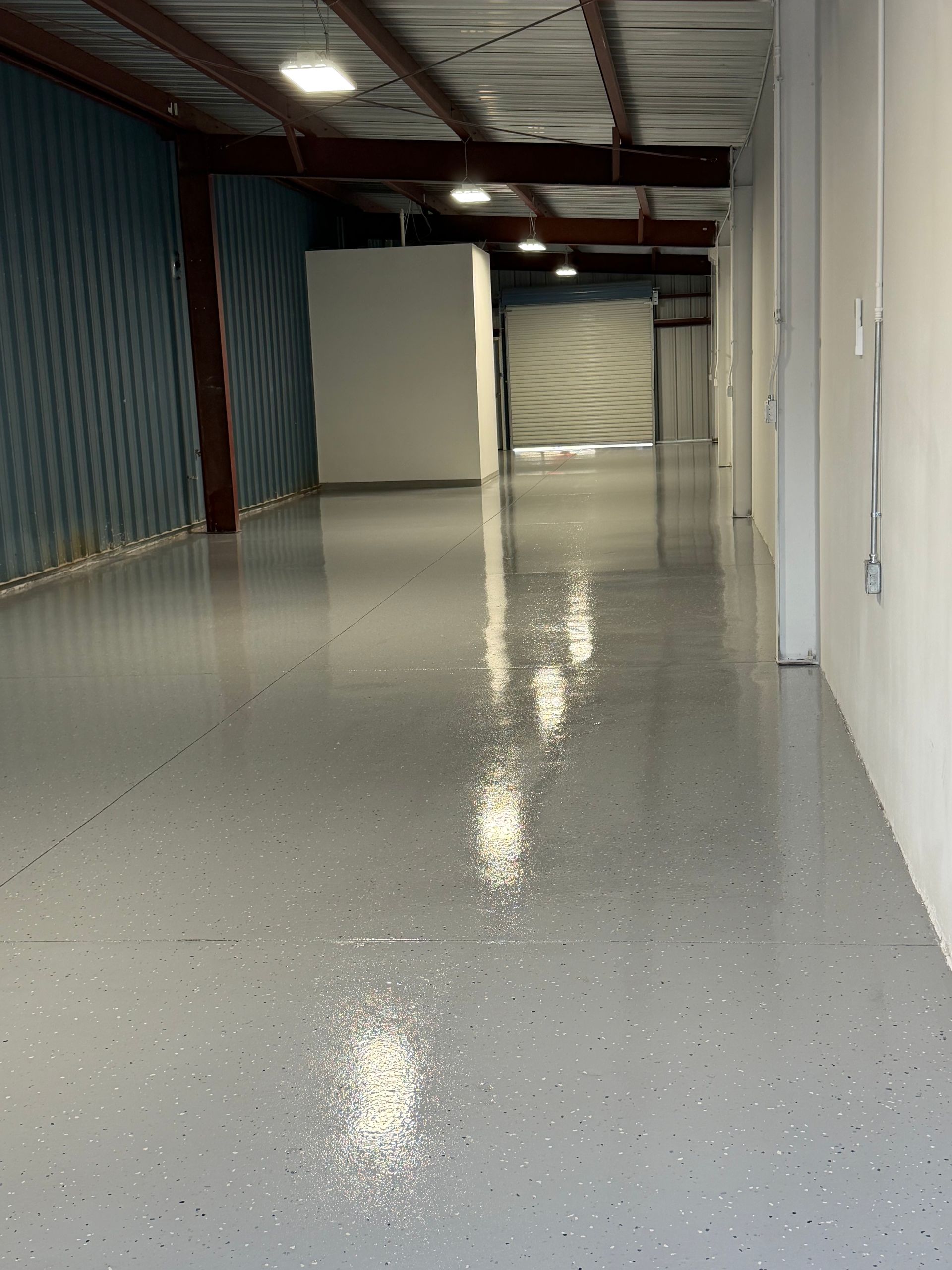 Empty industrial hallway with glossy gray floor, blue corrugated wall, and white partition walls