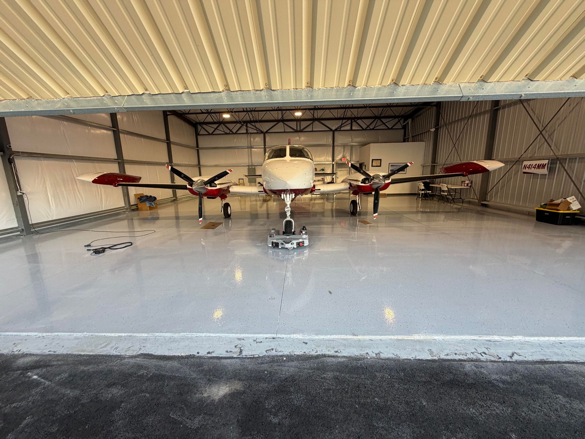 Twin-engine airplane parked in a hangar, centered in a wide open bay with polished floor.