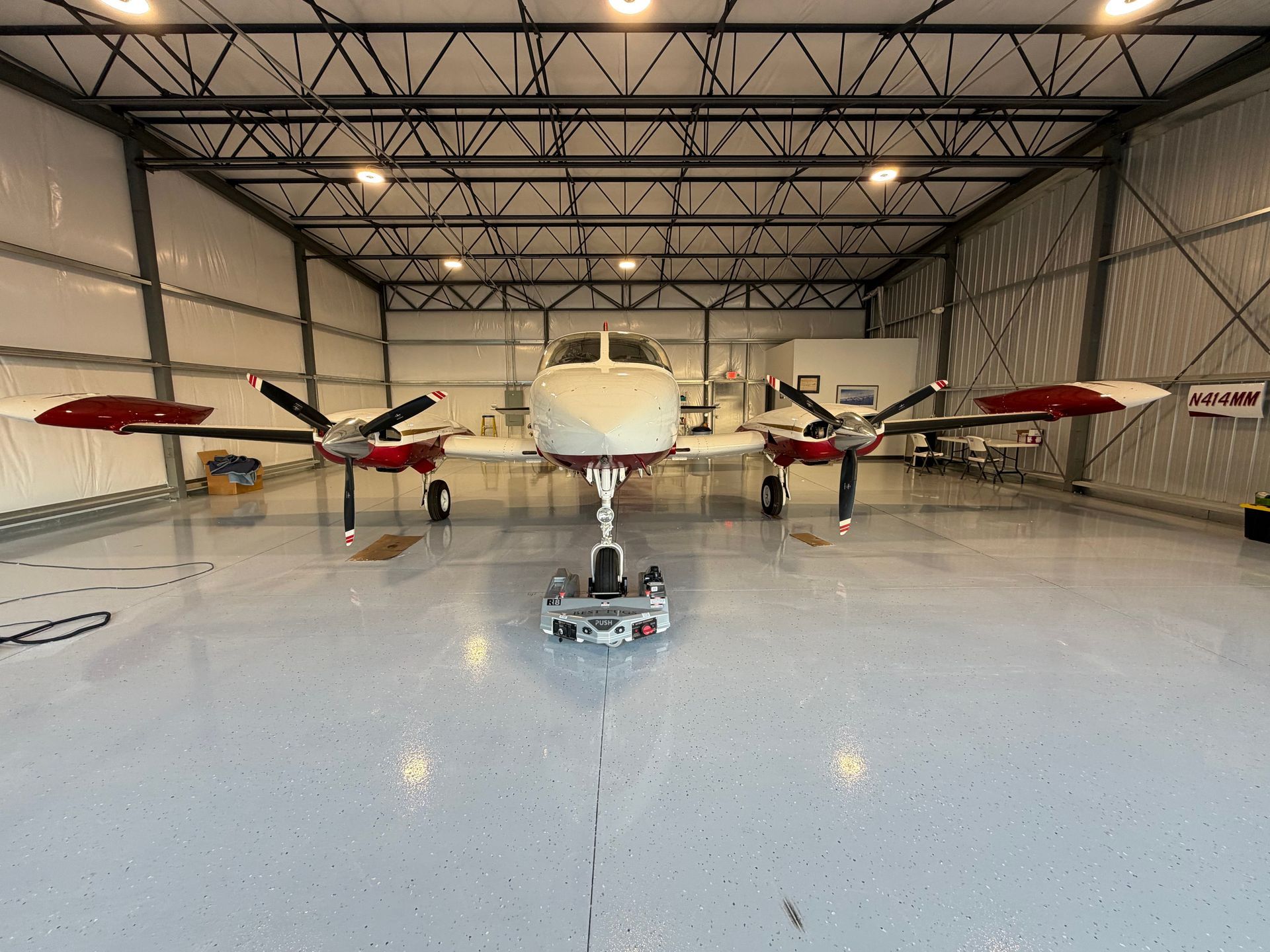 Twin-engine propeller airplane in a hangar, viewed head-on, with red-tipped wings and a glossy floor.