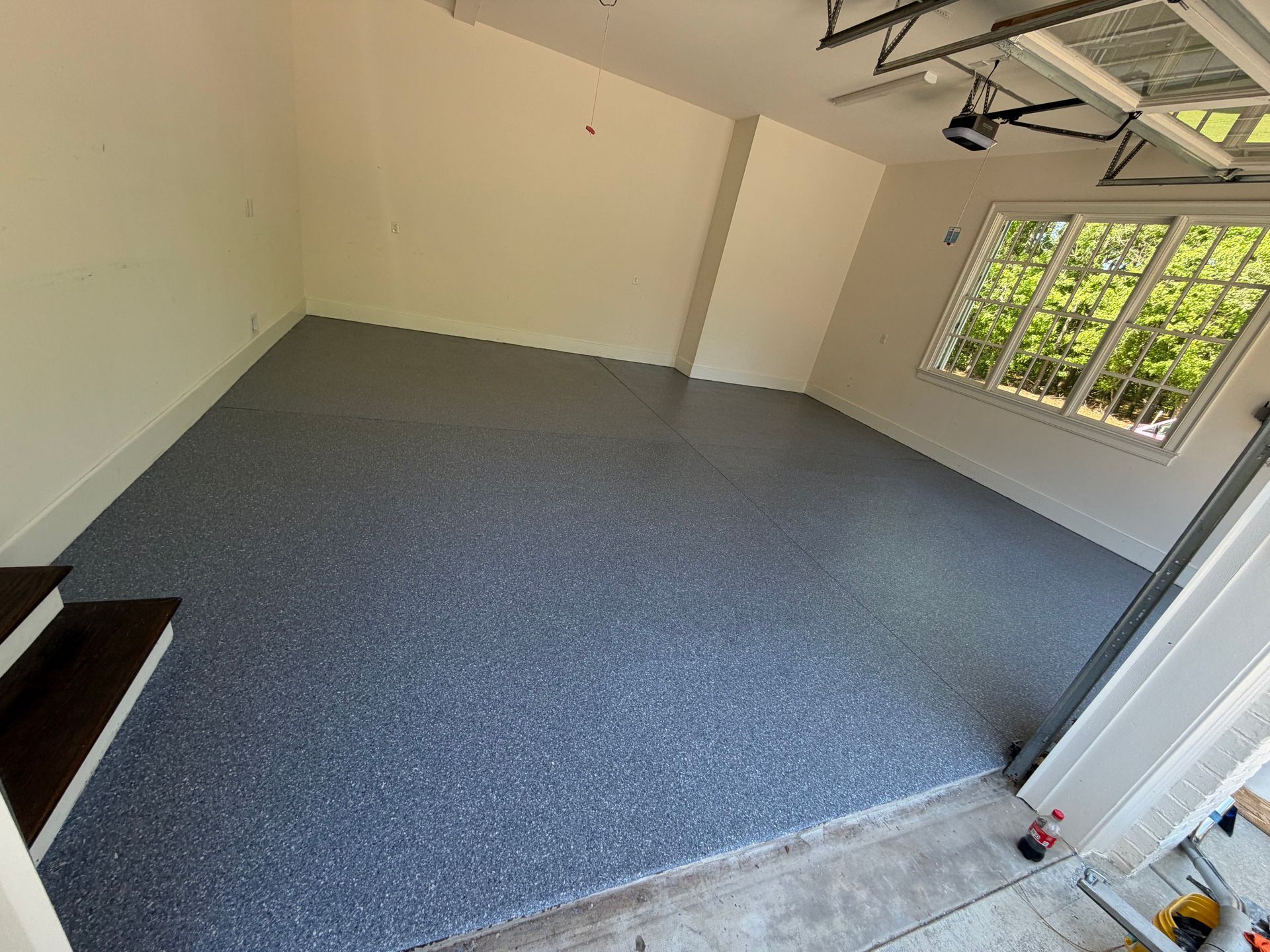 Empty carpeted room with beige walls, large window, and garage-style door opening