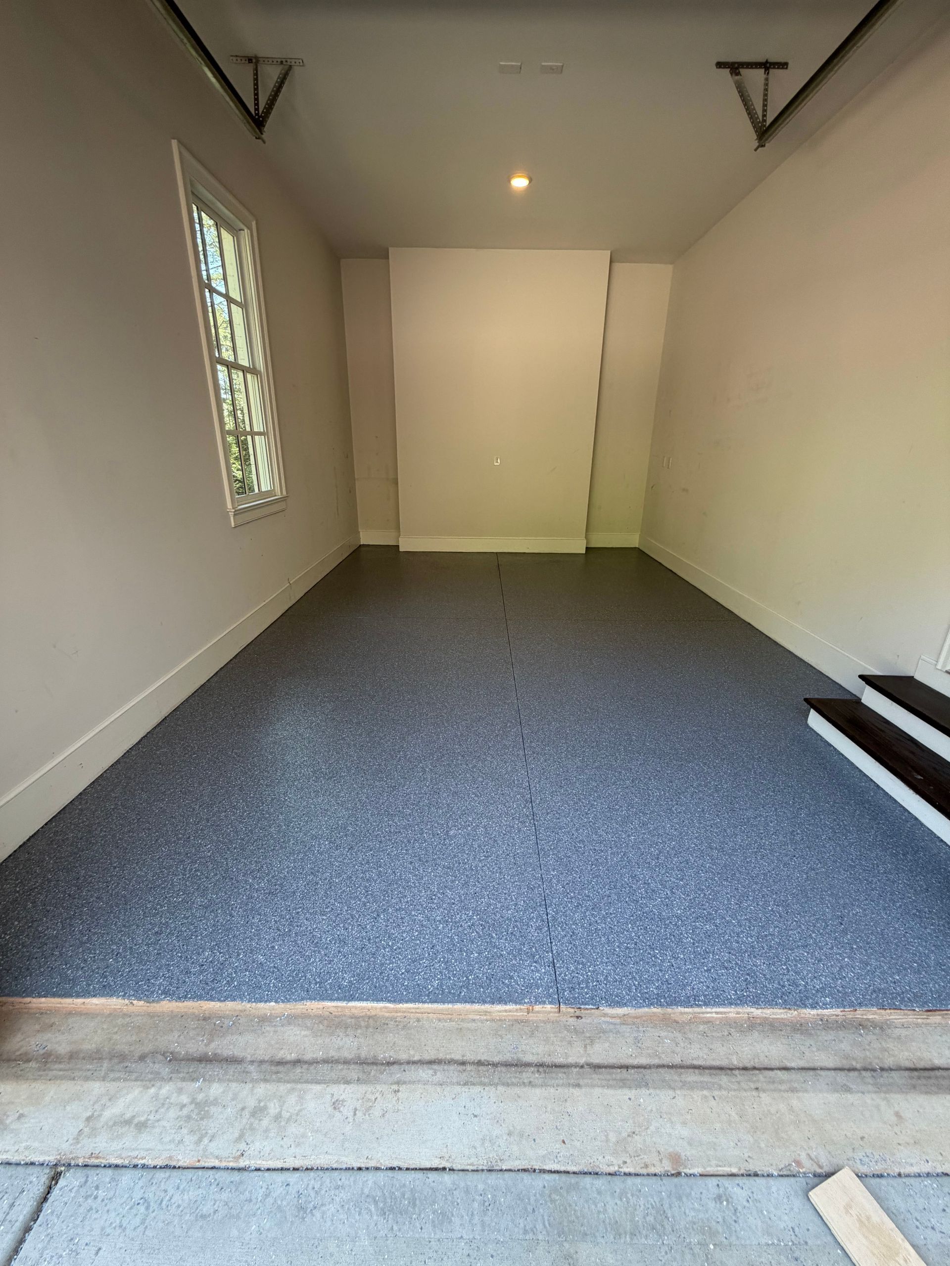 Empty carpeted basement room with white walls, small window, and stairs at the right edge
