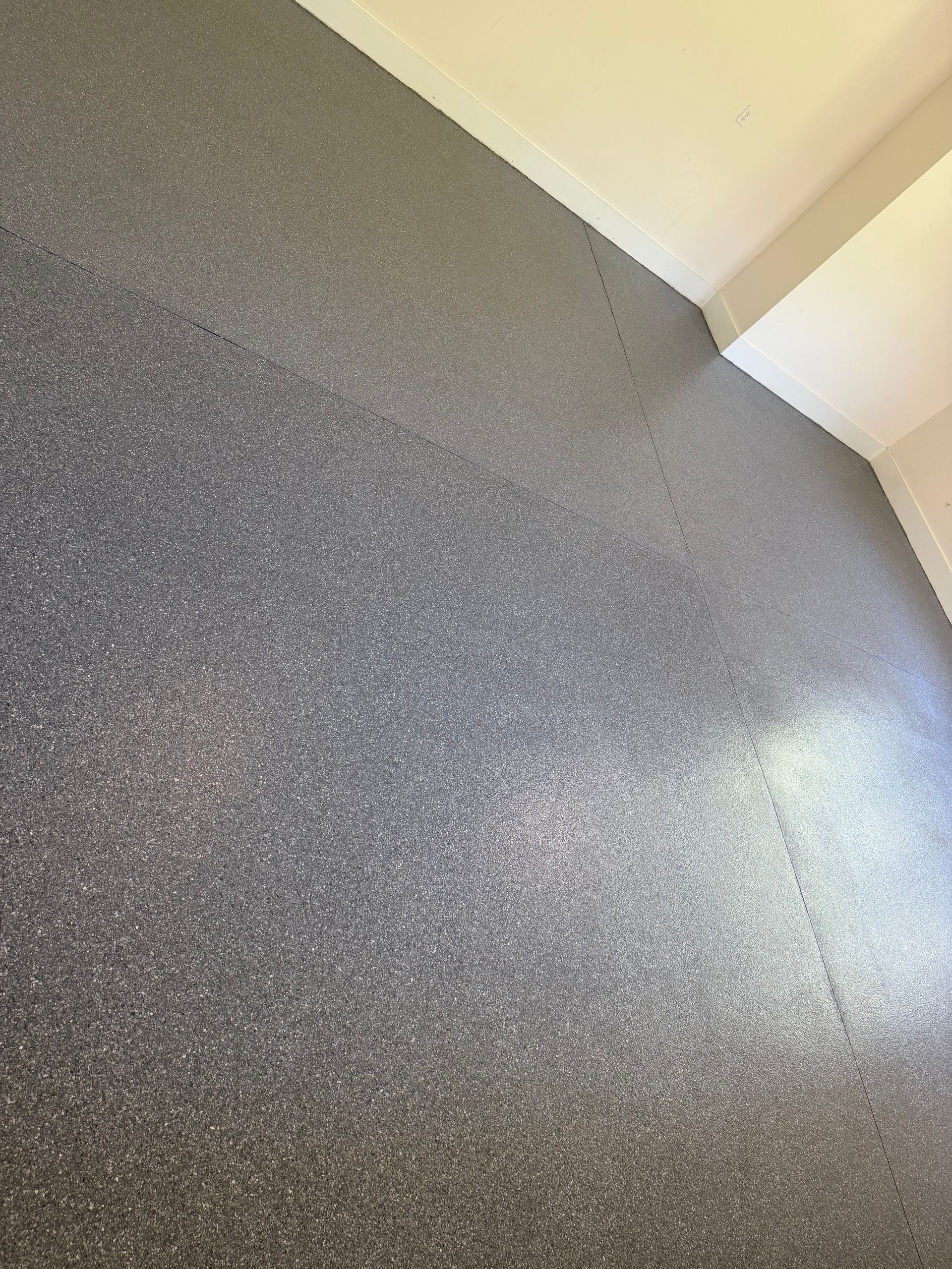 Close-up of a speckled gray floor meeting a white wall corner with bright light reflection