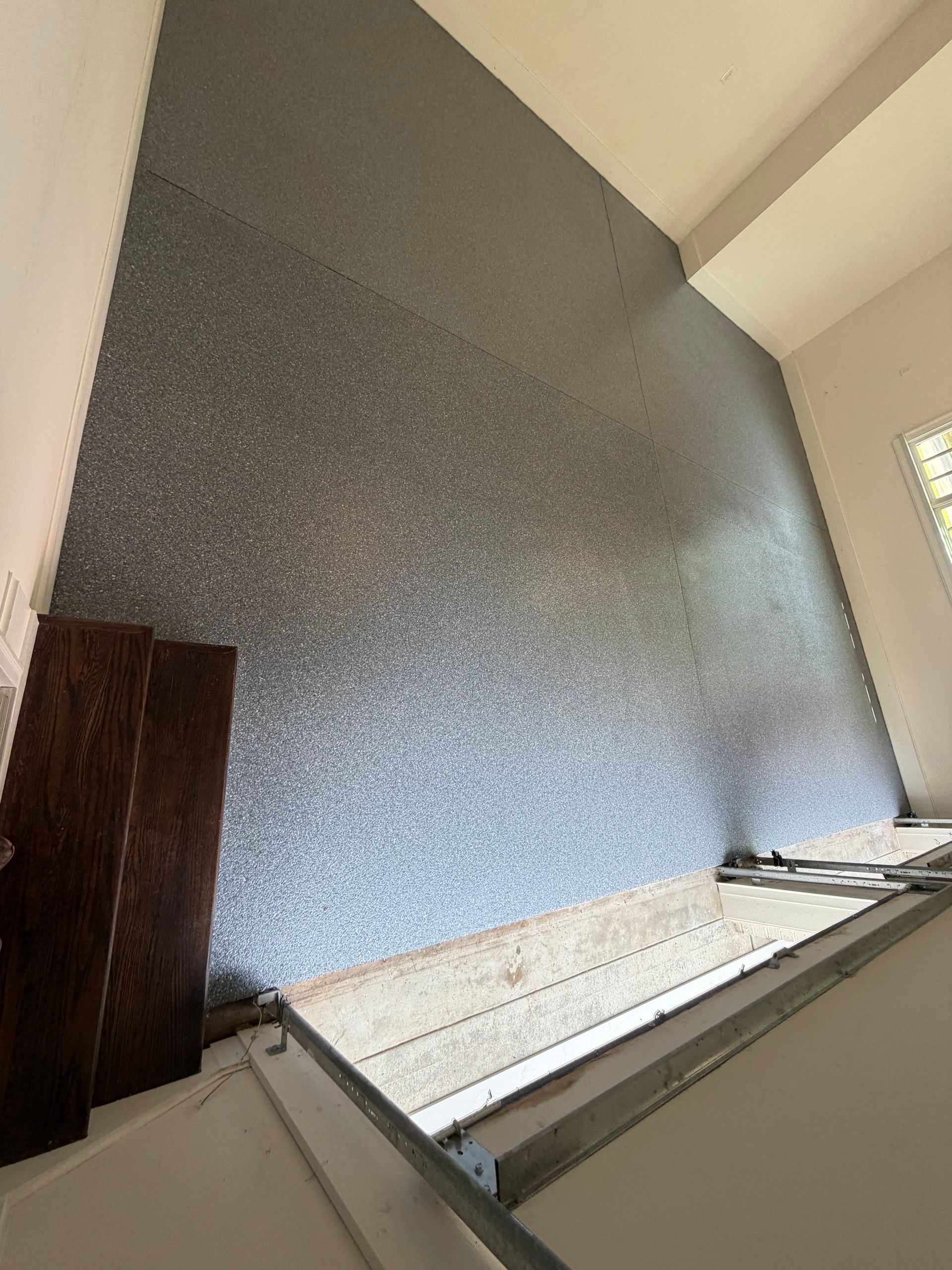 Tall textured gray wall in an interior stairwell with a wooden panel and window light.