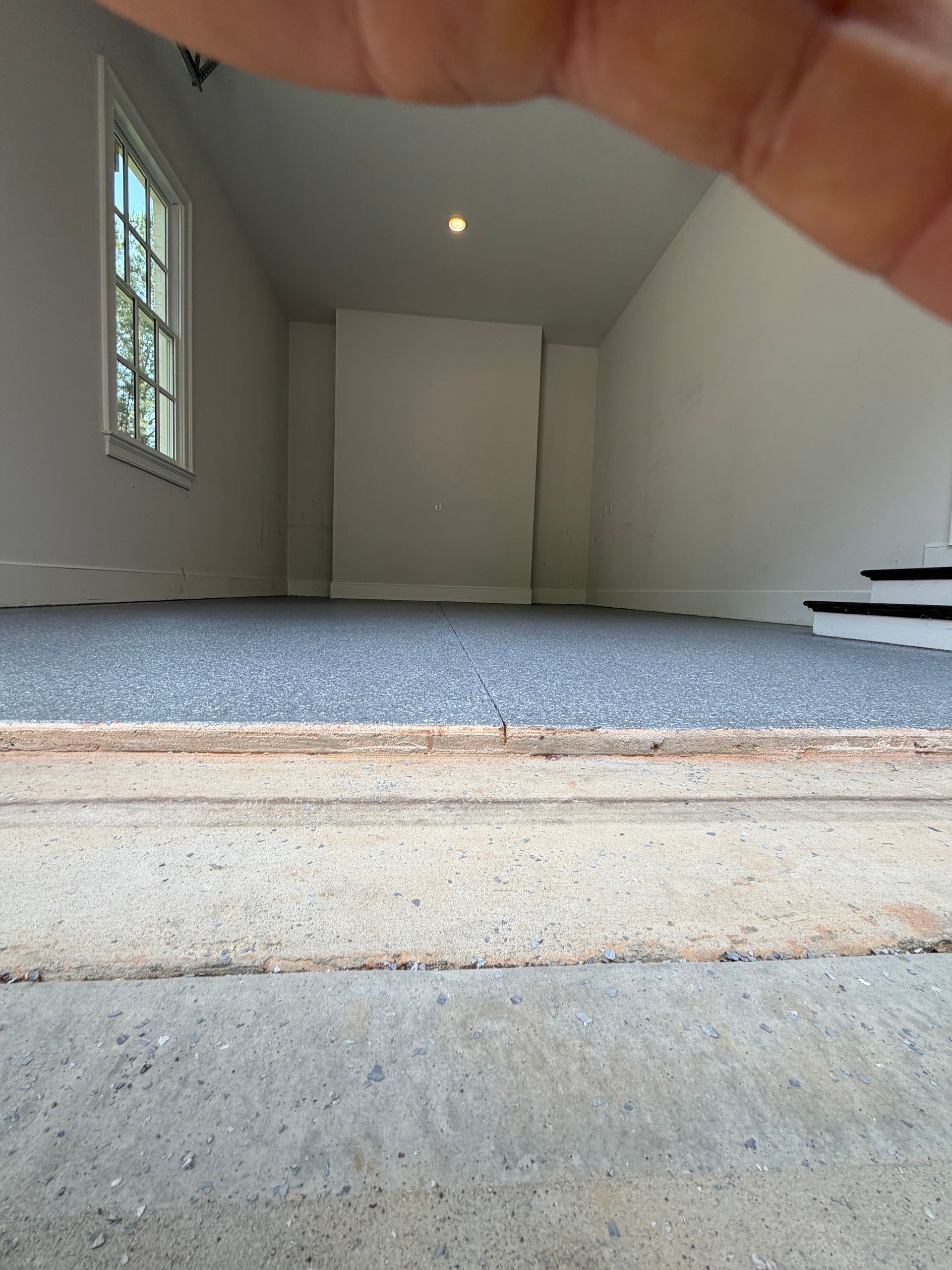 Empty carpeted room with white walls, a window on the left, and stairs on the right.