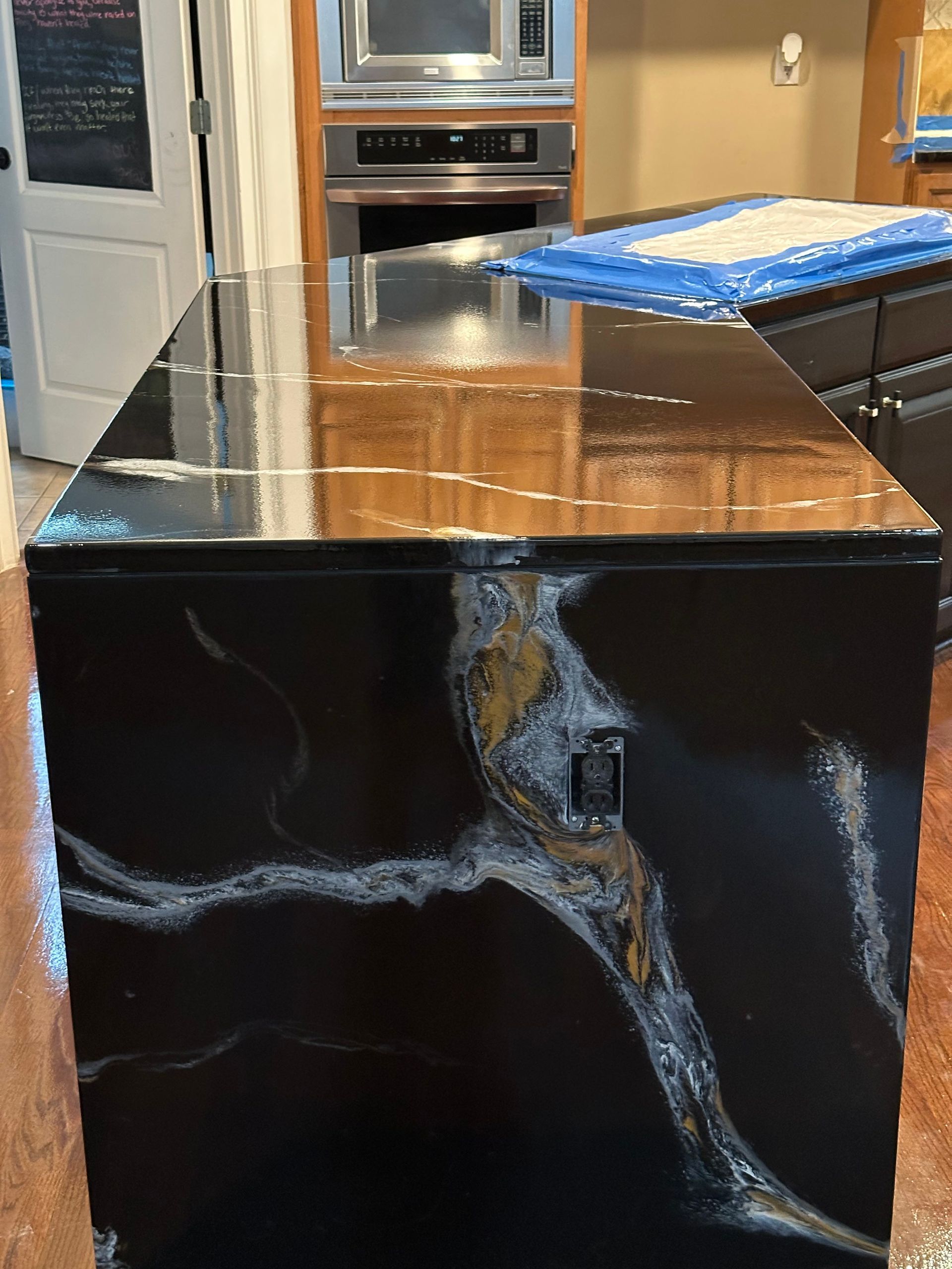 Black marble kitchen island with a glossy wooden top and a blue padded item on the right side.