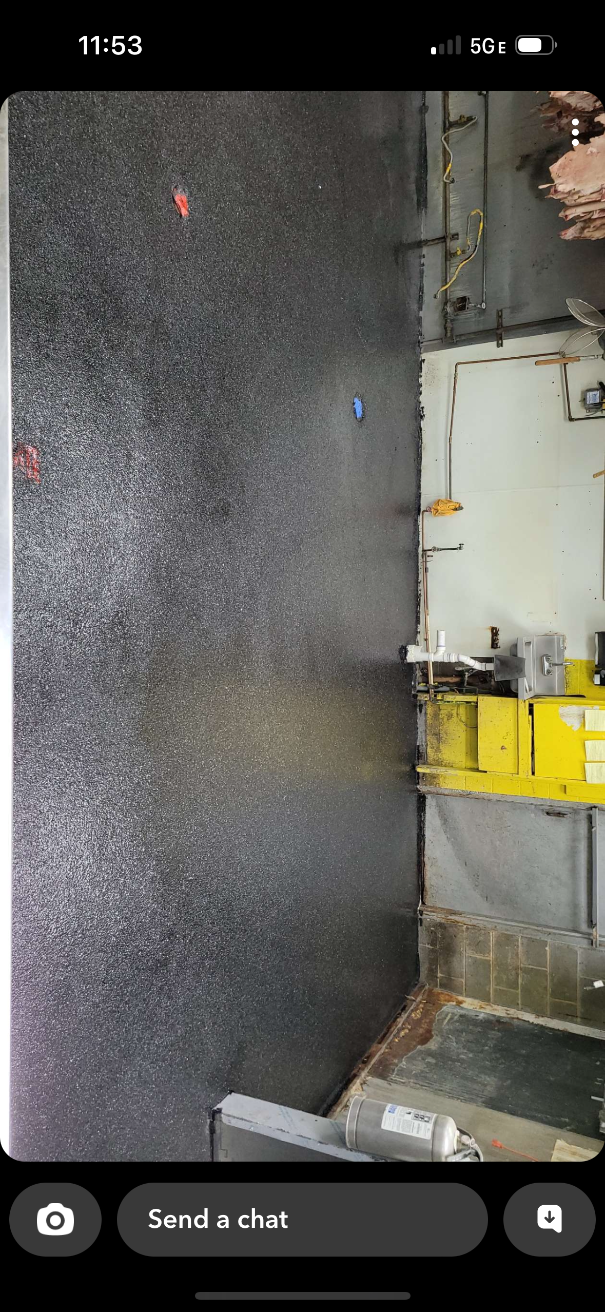 Dark gravel lot beside a white industrial building and yellow equipment, with a small red marker on the ground.