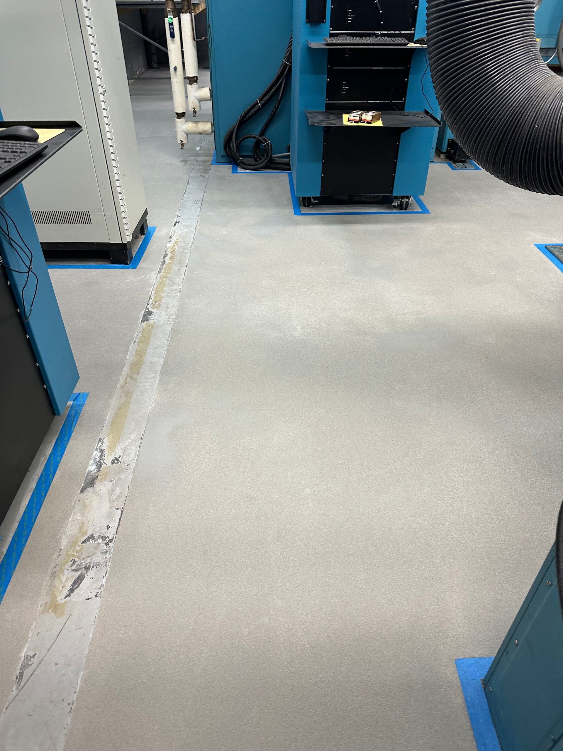 Industrial walkway between blue machines with a gray floor and visible cables.