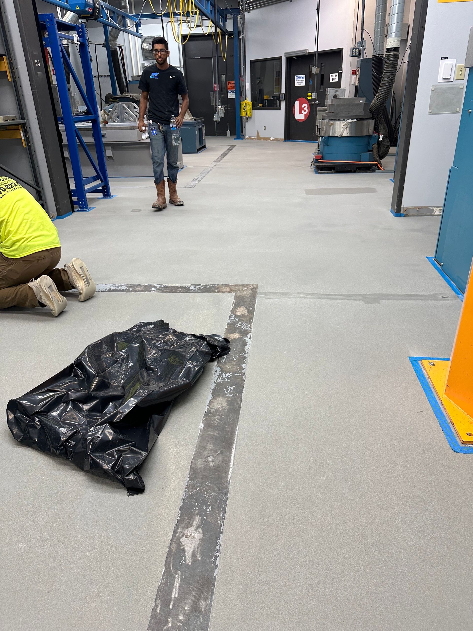 Industrial hallway with workers, a black tarp on the floor, and blue equipment along the walls.