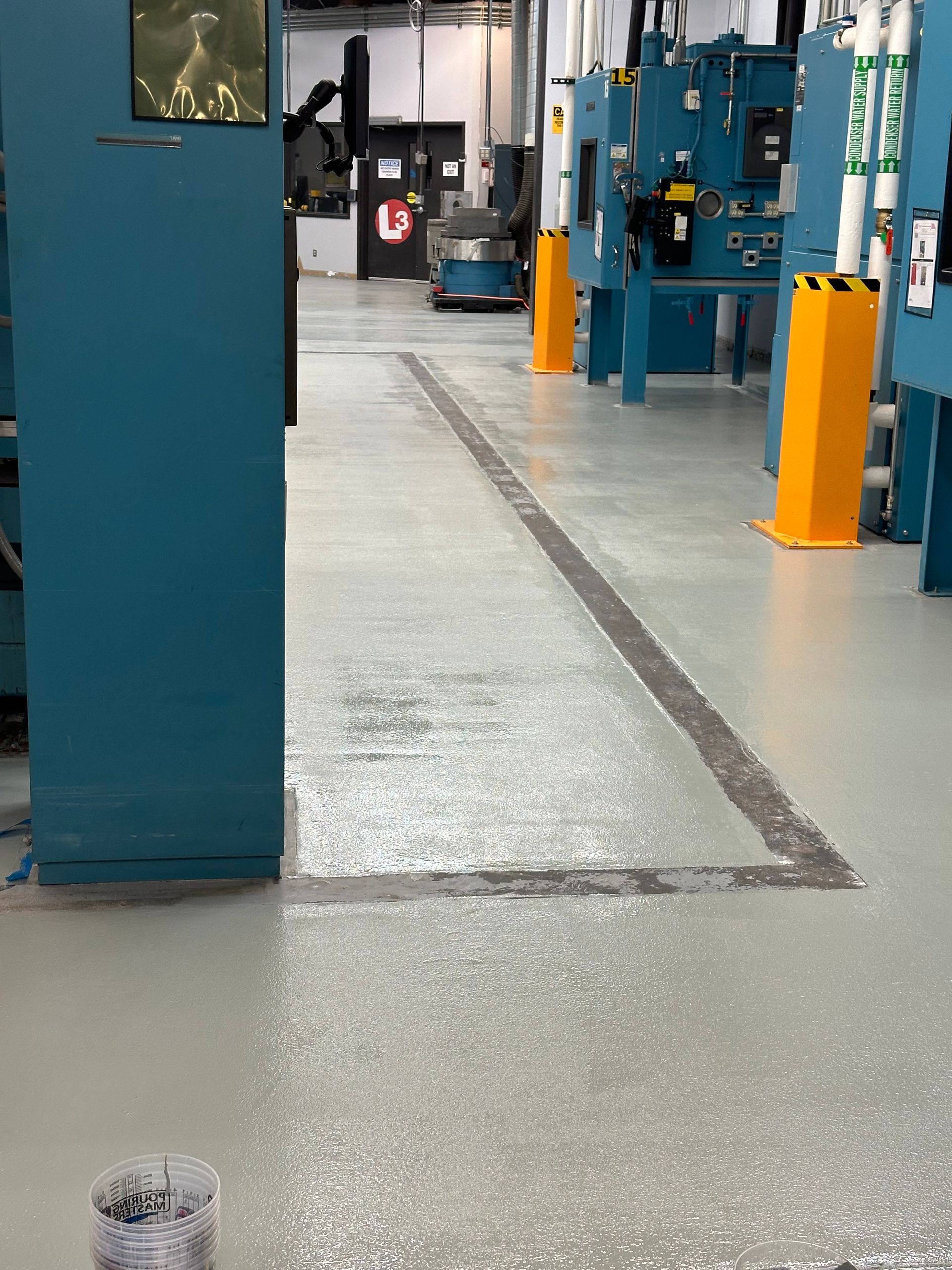 Industrial workshop aisle with blue machinery and yellow bollards on a gray floor