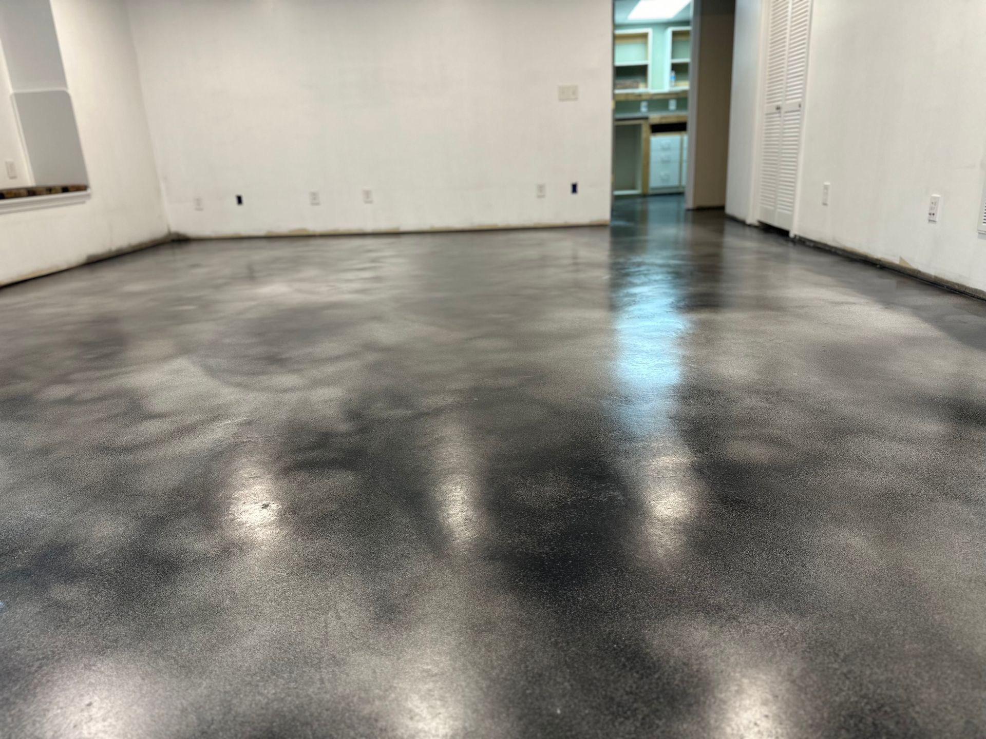 Shiny dark floor with wet-looking patches beside a white wall and door vents indoors