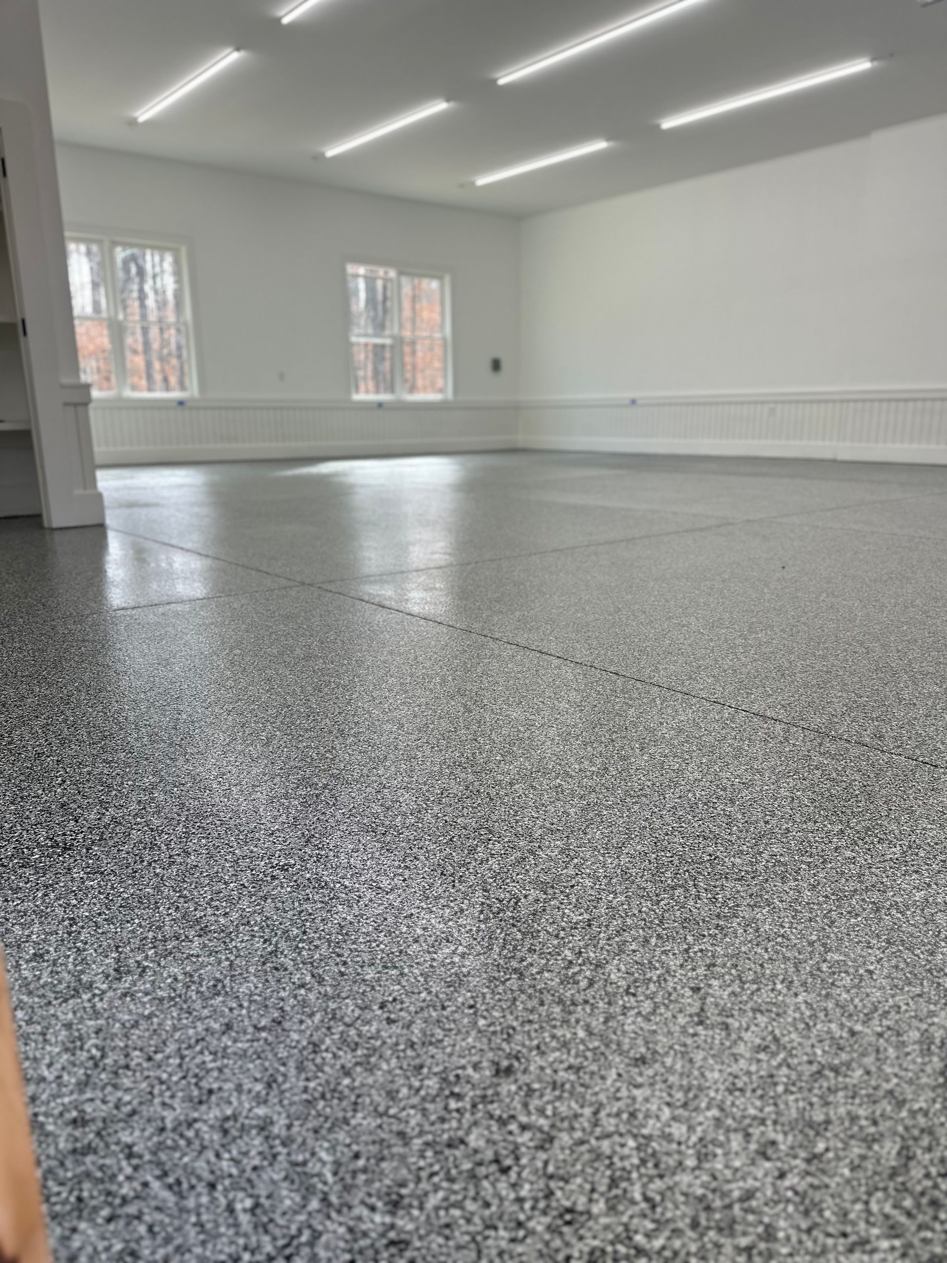 Empty bright room with white walls, windows, and speckled gray floor coating