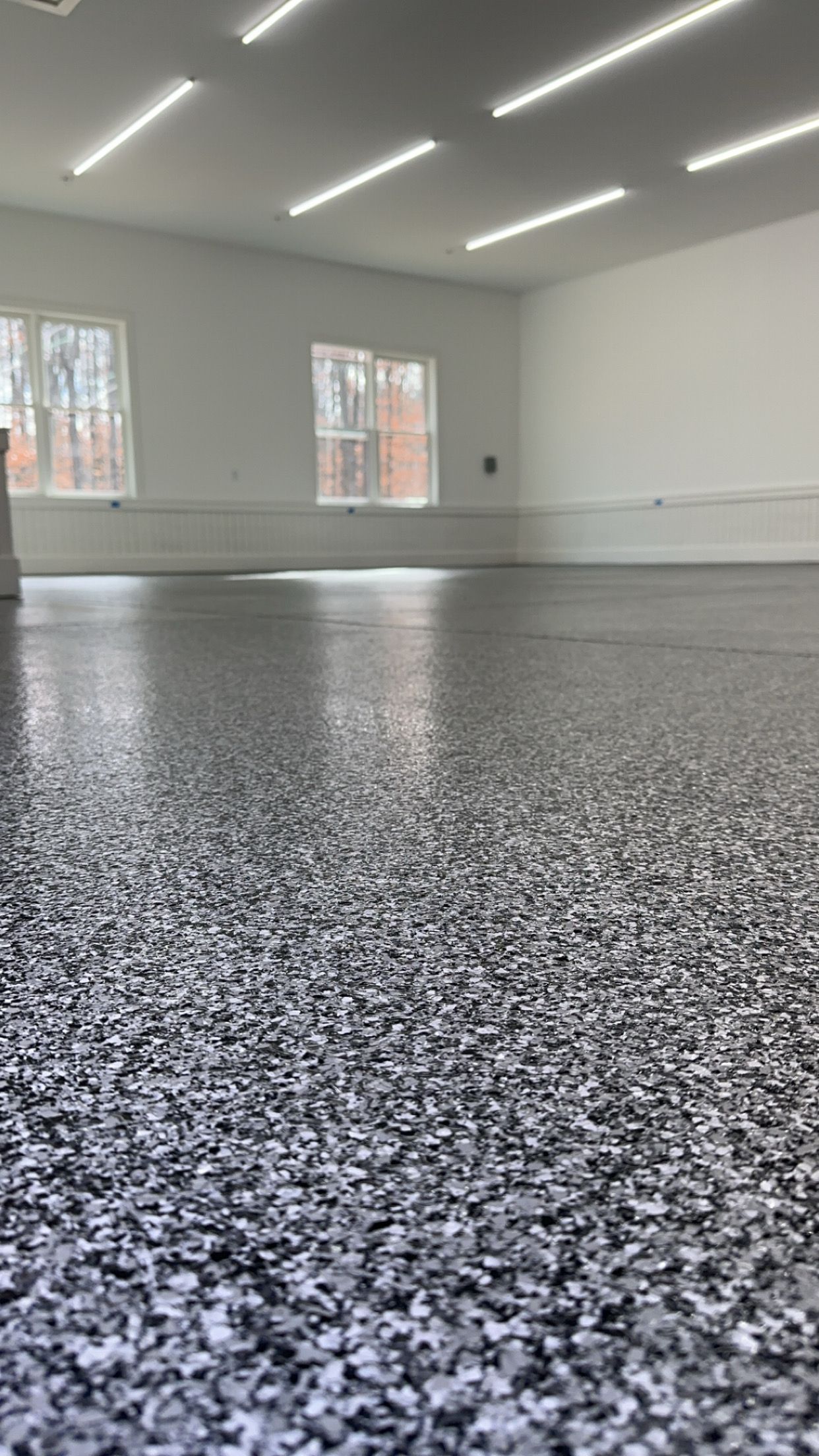 Empty bright garage with speckled epoxy floor, white walls, and windows letting in daylight.