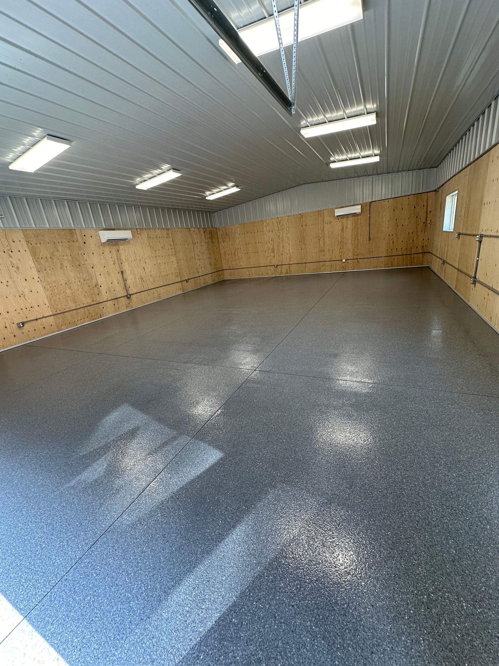 Empty industrial room with tan walls and a speckled gray floor under fluorescent ceiling lights