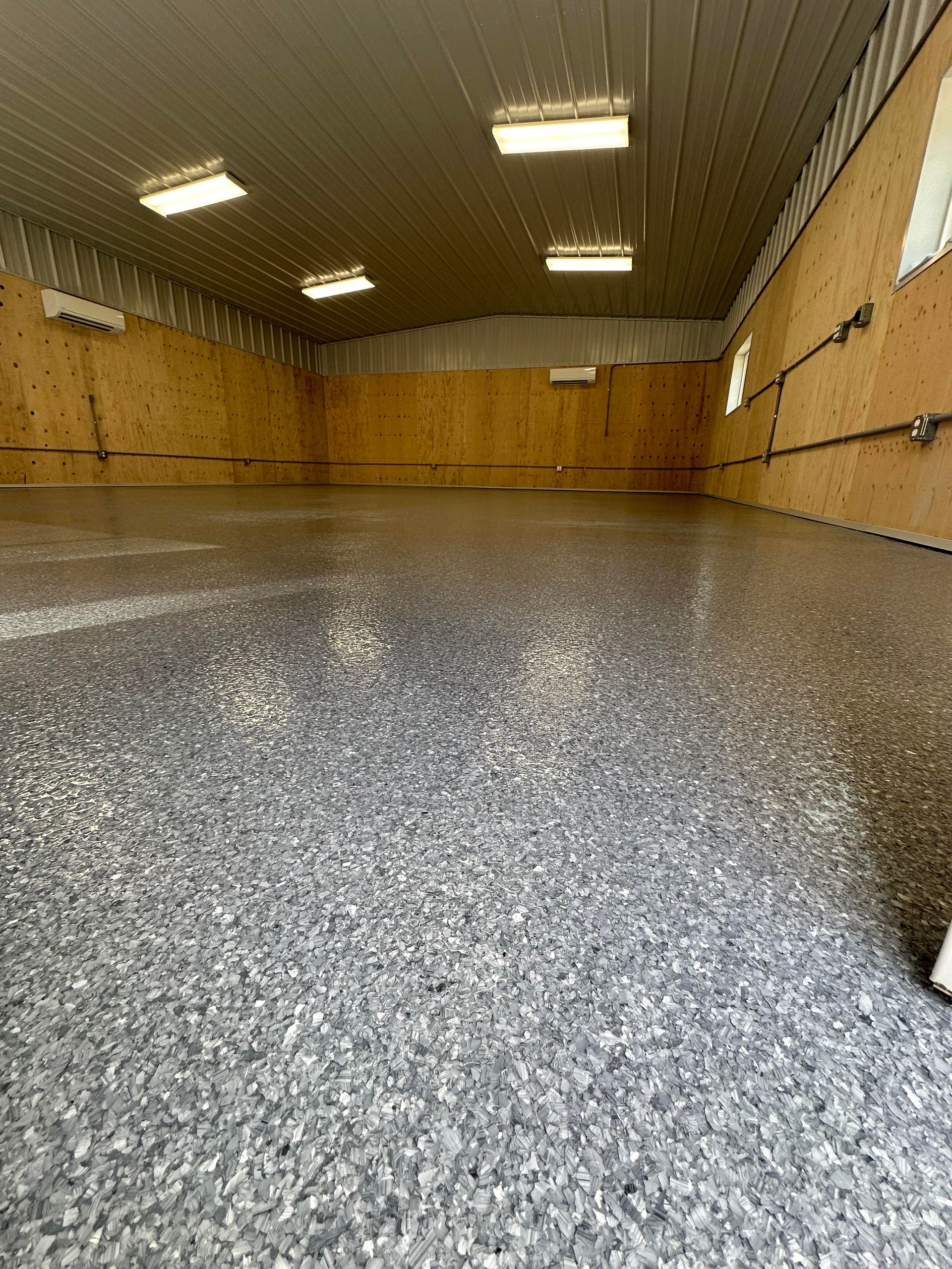Empty warehouse with speckled epoxy floor, wooden walls, and fluorescent ceiling lights