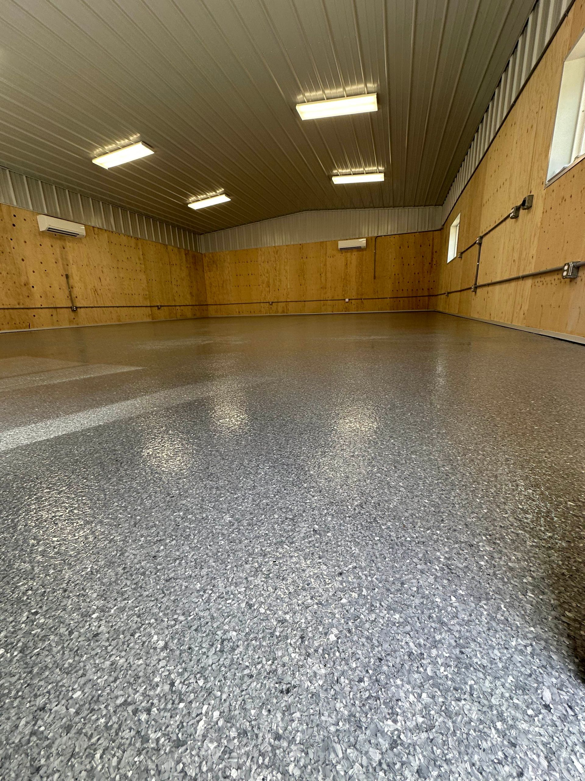 Empty indoor room with wood-paneled walls, speckled floor, and overhead fluorescent lights