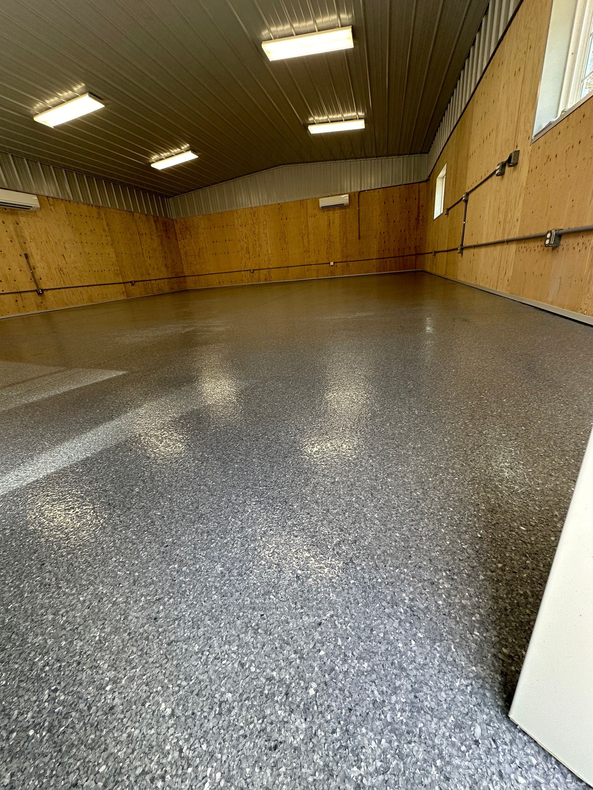 Empty indoor room with speckled epoxy floor, wood-paneled walls, and fluorescent ceiling lights.