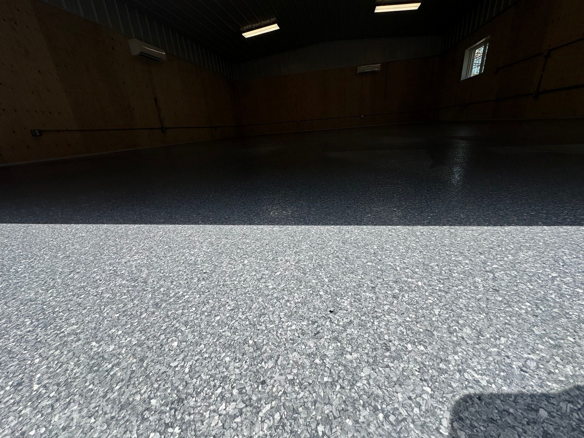 Dark indoor room with a bright, textured floor and a small window on the right.