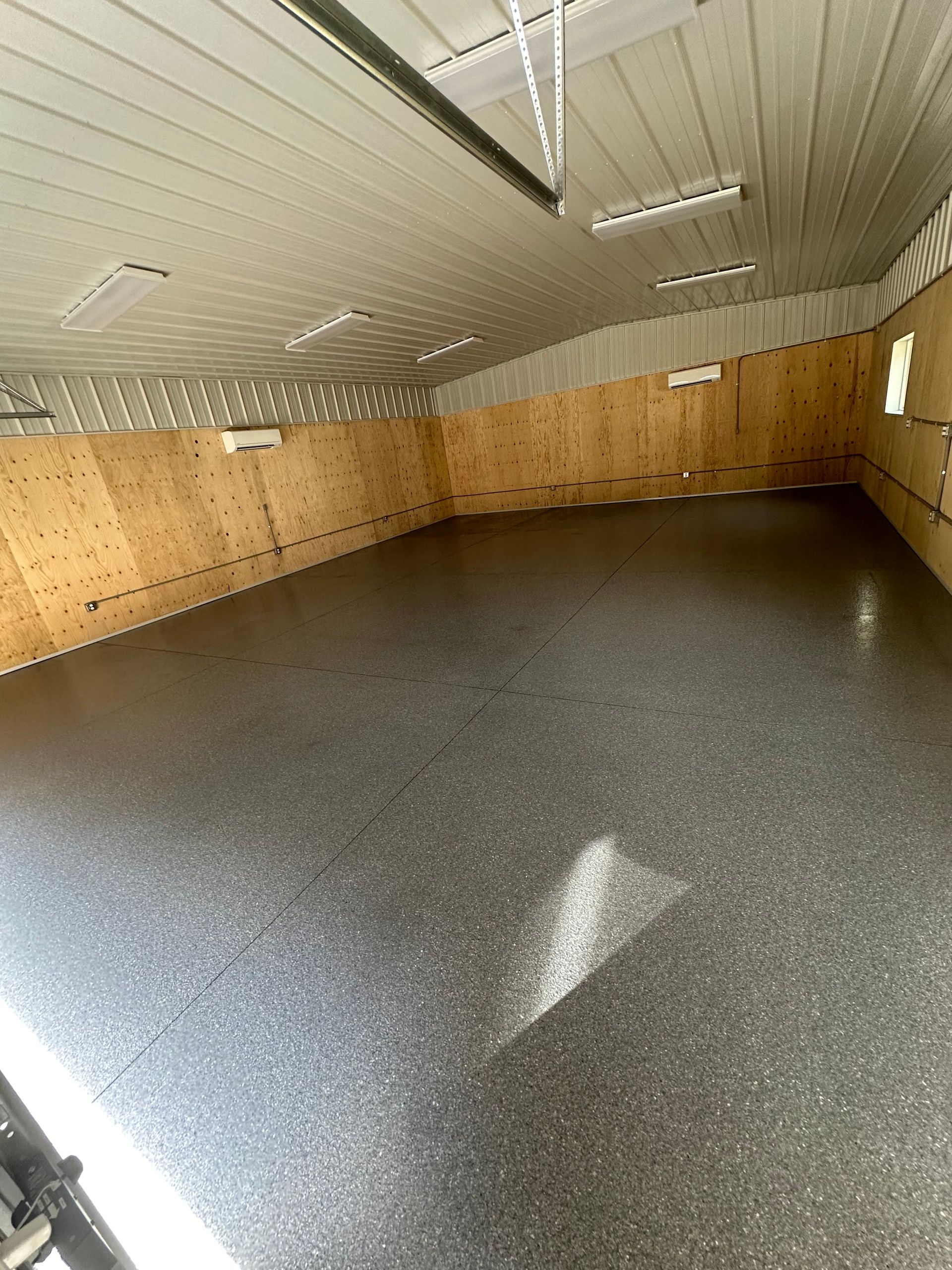 Empty workshop with wood-paneled walls, white ceiling lights, and a speckled gray floor.