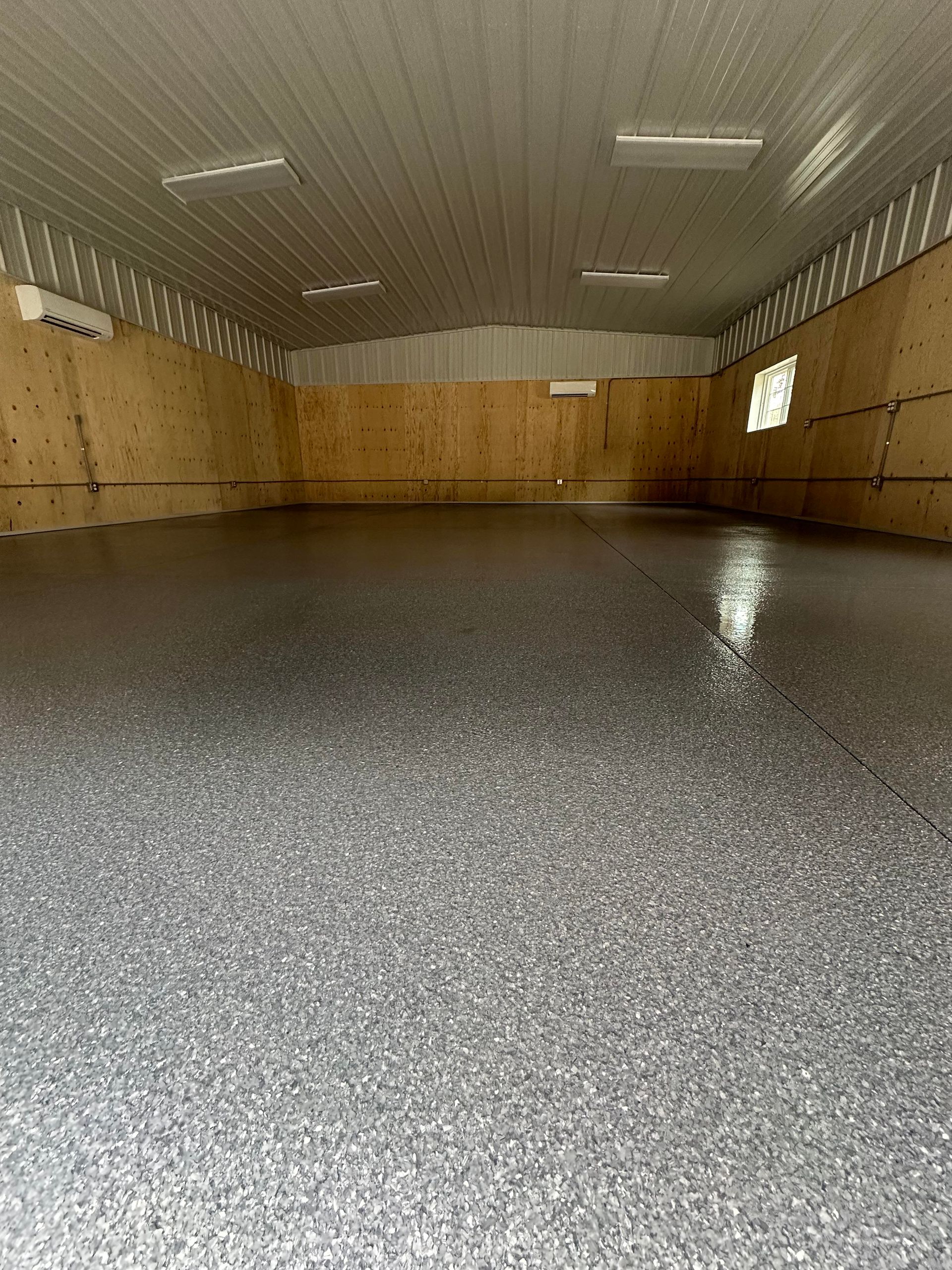Empty indoor room with wood-paneled walls, gray speckled floor, and a curved metal ceiling.