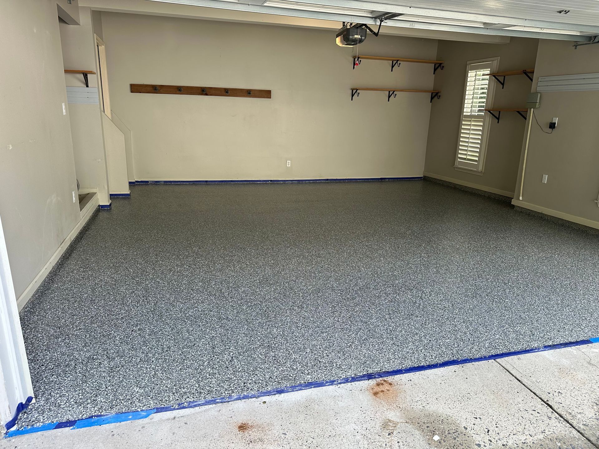 Empty garage with speckled gray floor, white walls, and a side door with window blinds.