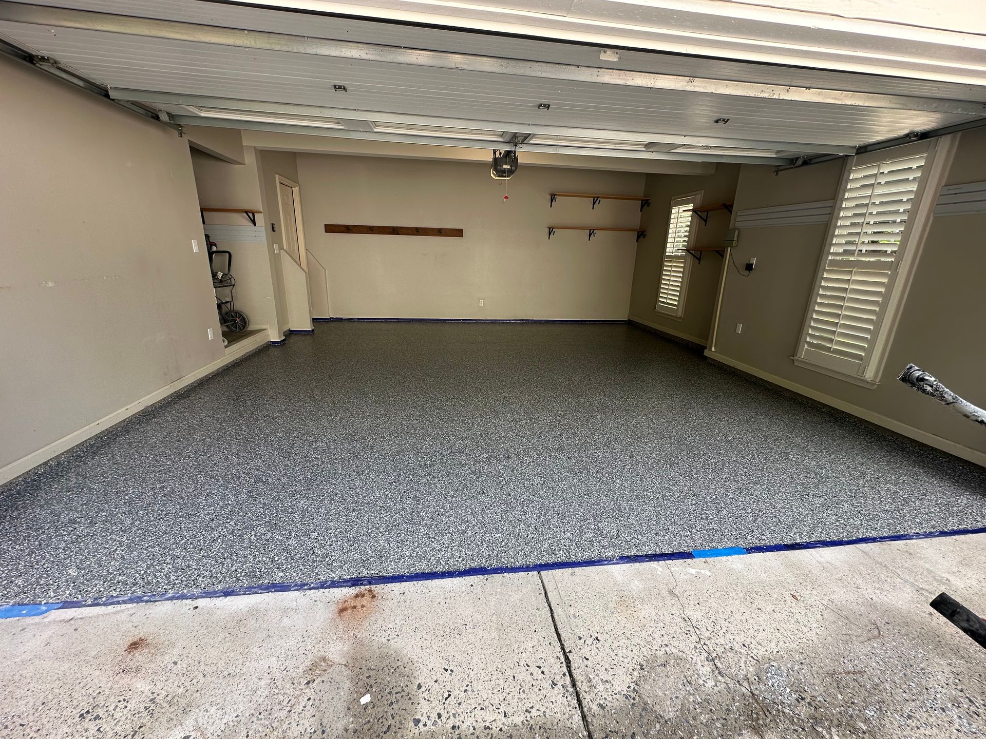 Empty garage with gray speckled floor, beige walls, and an open door to a concrete driveway.