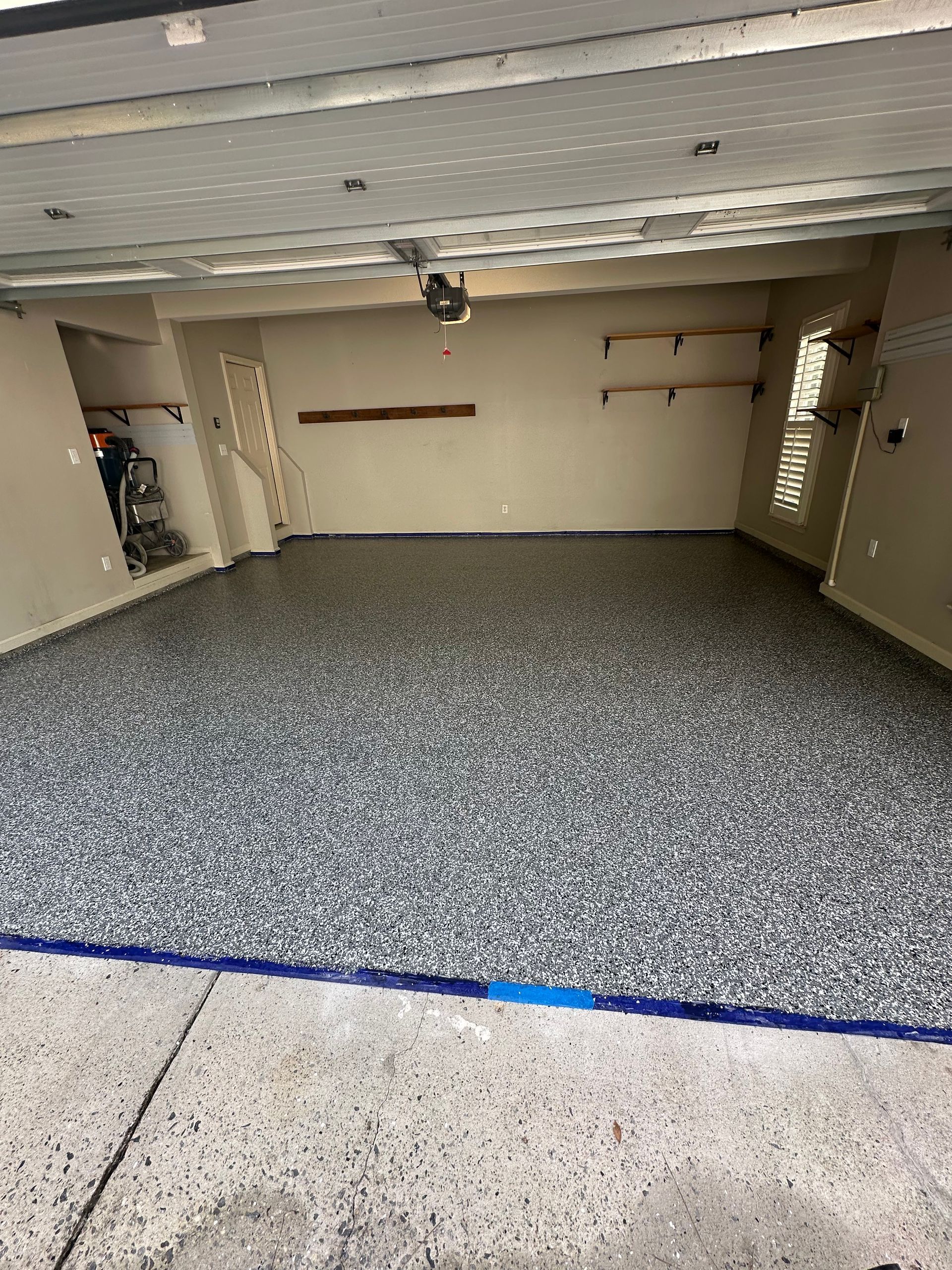 Empty garage interior with gray speckled floor, beige walls, and open shelving on the right.
