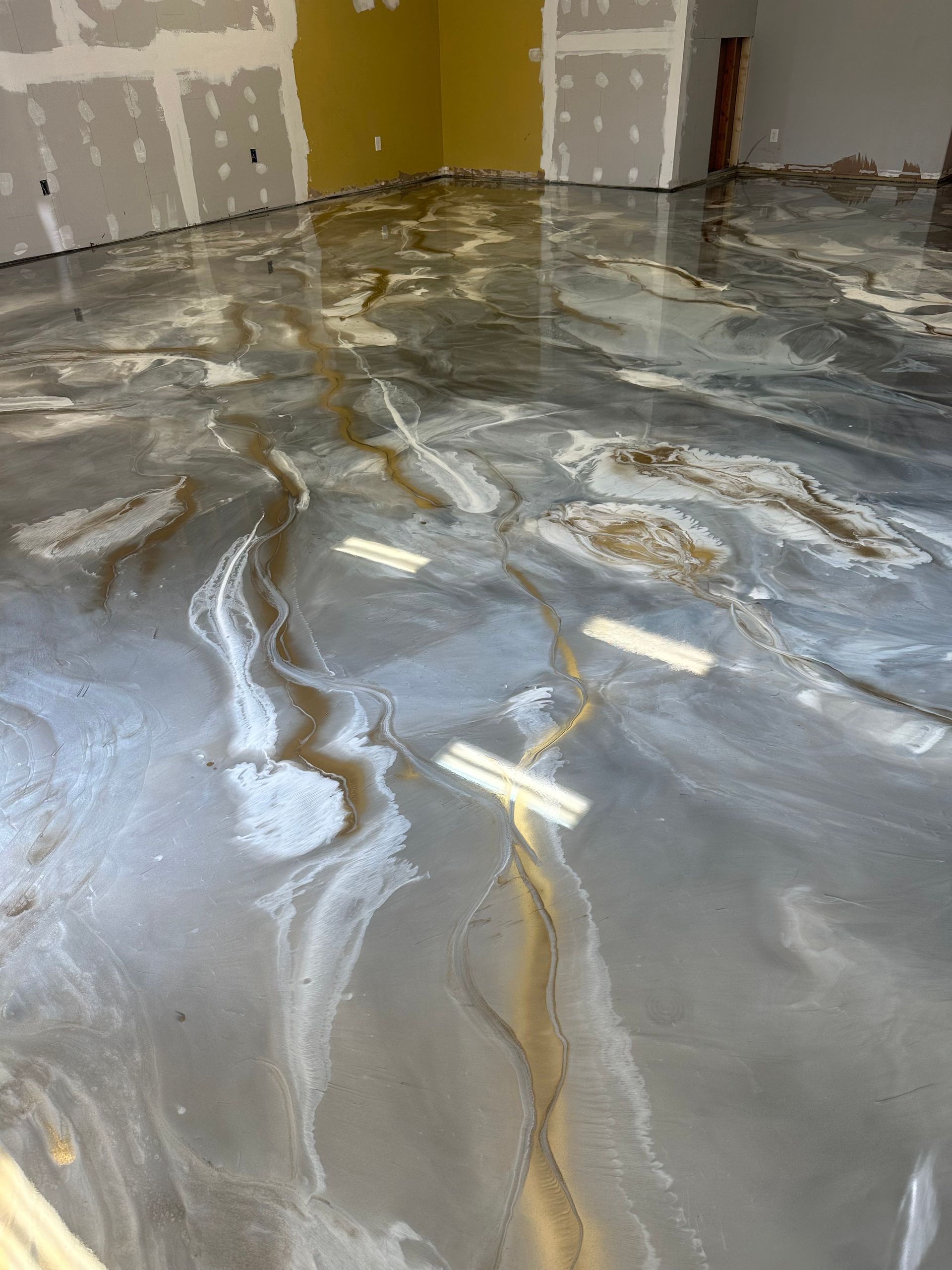Wet epoxy-coated garage floor with gray, white, and gold marbled swirls reflecting ceiling lights
