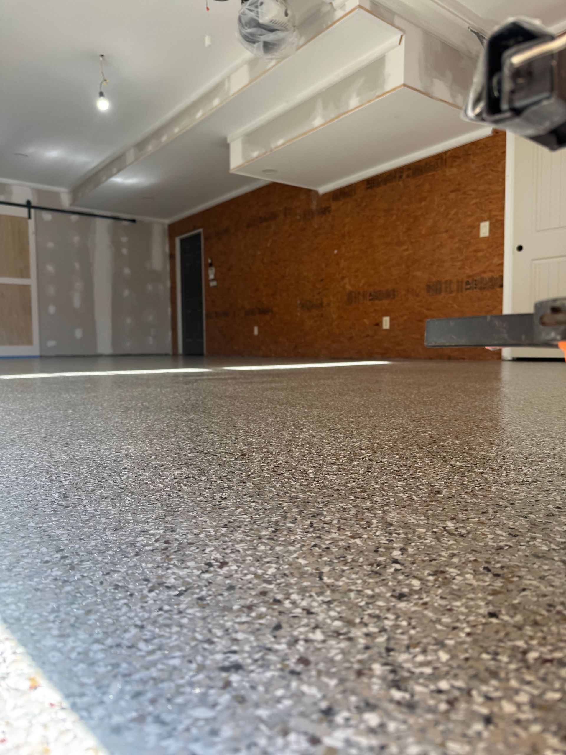 Empty garage with speckled epoxy floor, white ceiling, and brick wall.