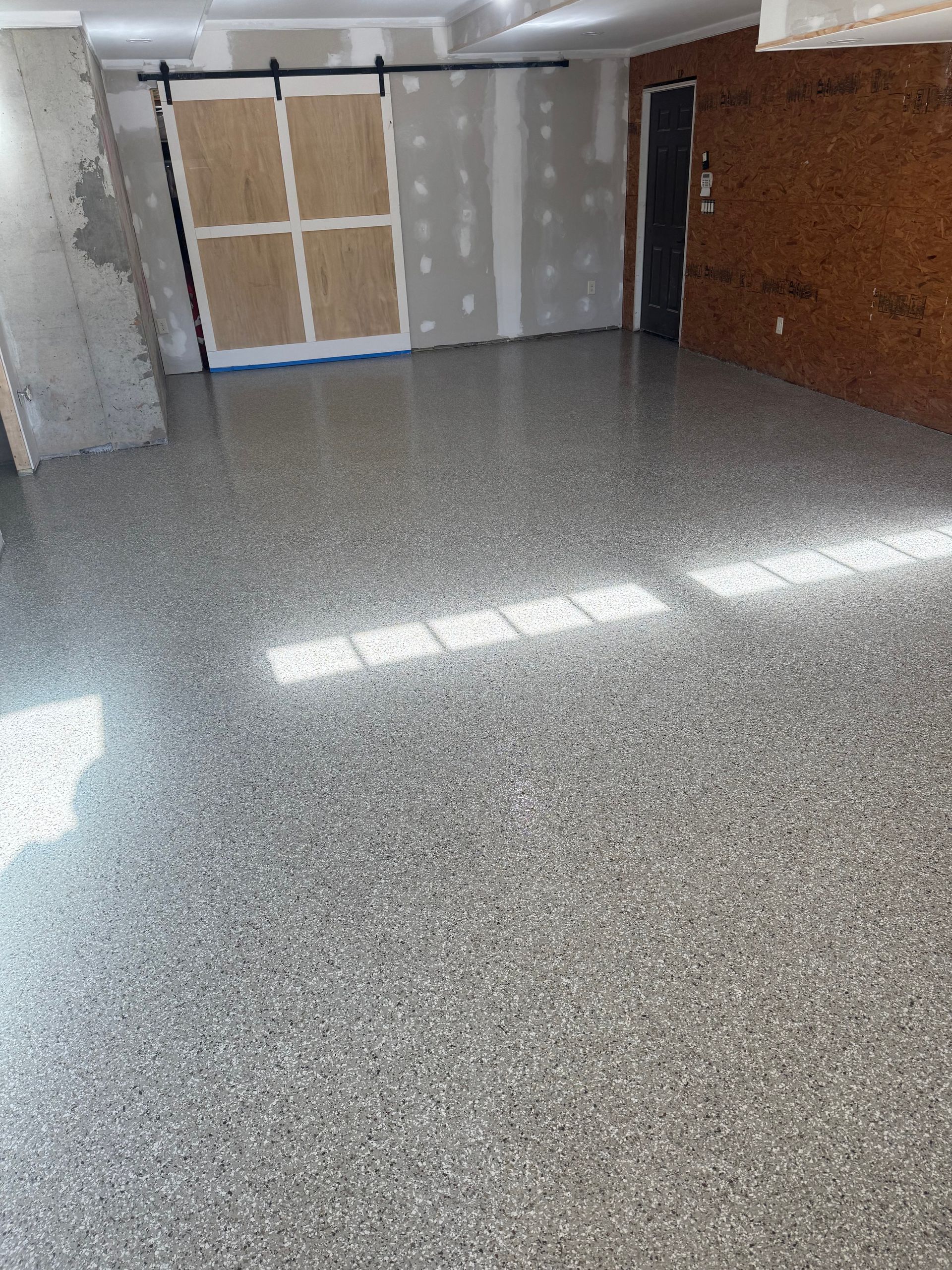 Empty unfinished room with gray speckled floor, drywall, and a covered door or window at the back.
