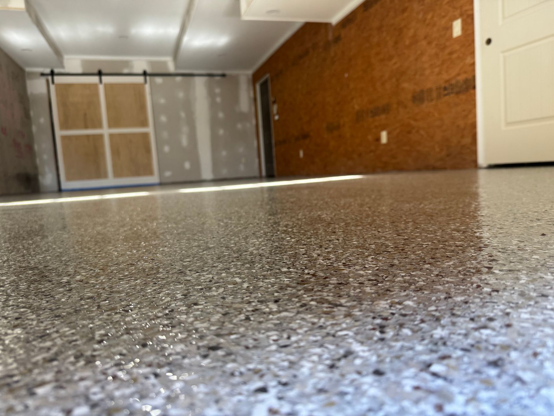Low-angle view of an empty garage with speckled floor, brick wall, and closed doors