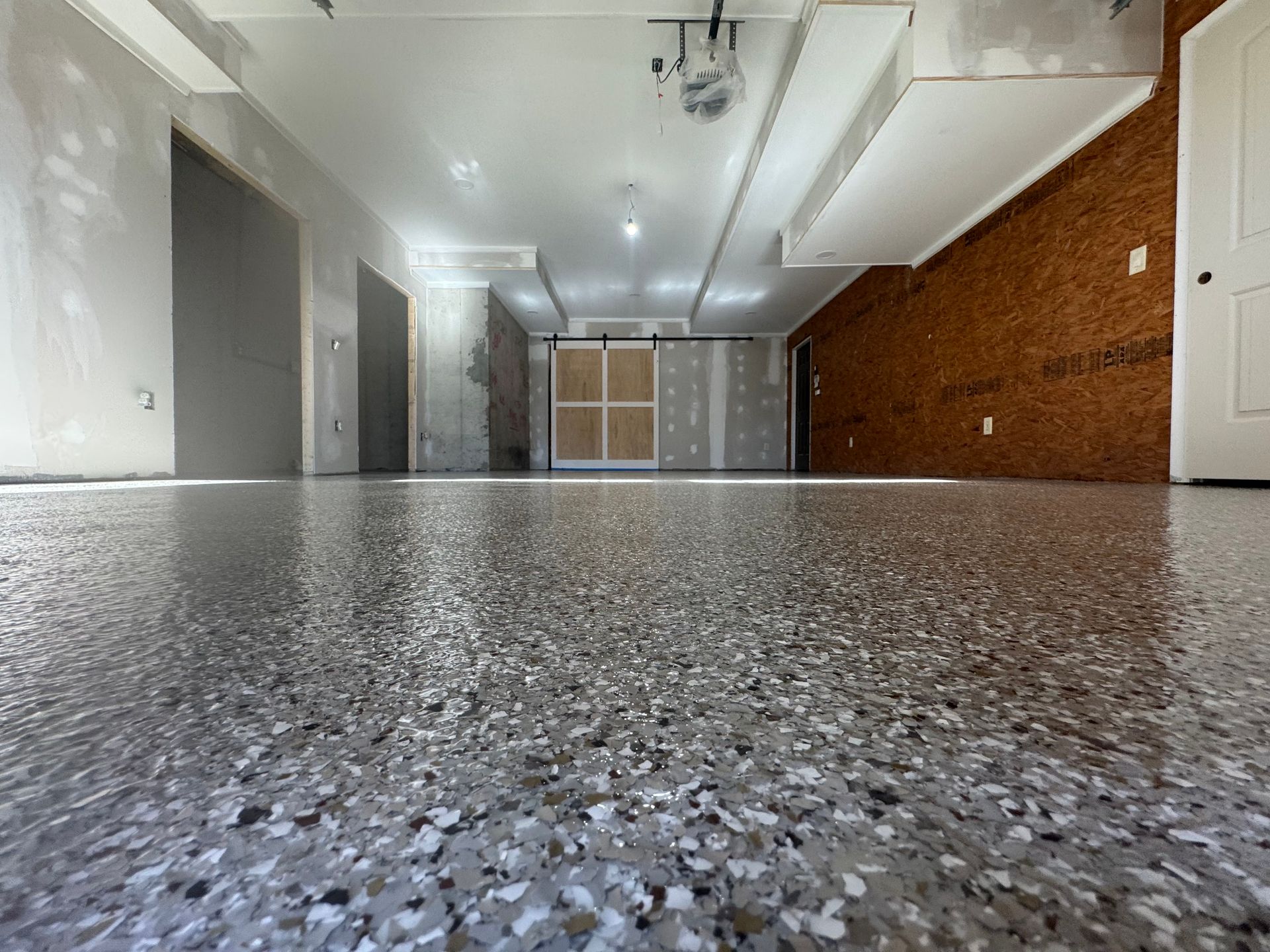 Low-angle view of a long empty hallway with speckled floor, white walls, and a corkboard on the right.