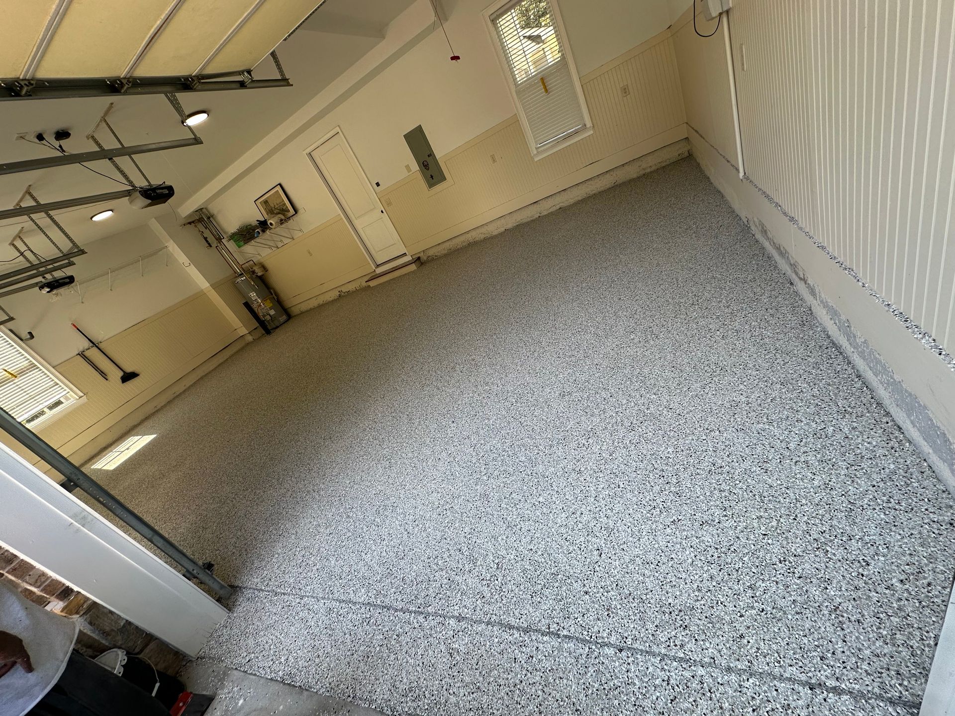 Empty garage interior with speckled floor, white walls, and a raised garage door.
