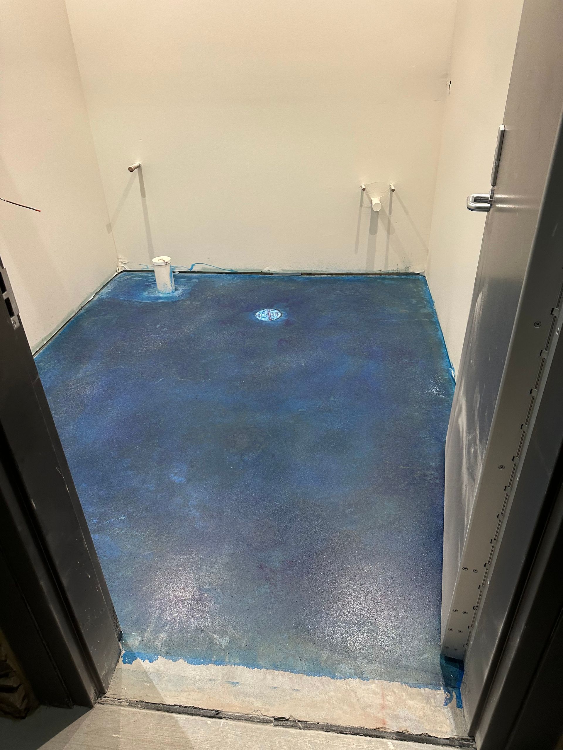 Small unfinished room with a blue floor and bare beige walls, viewed through a doorway.