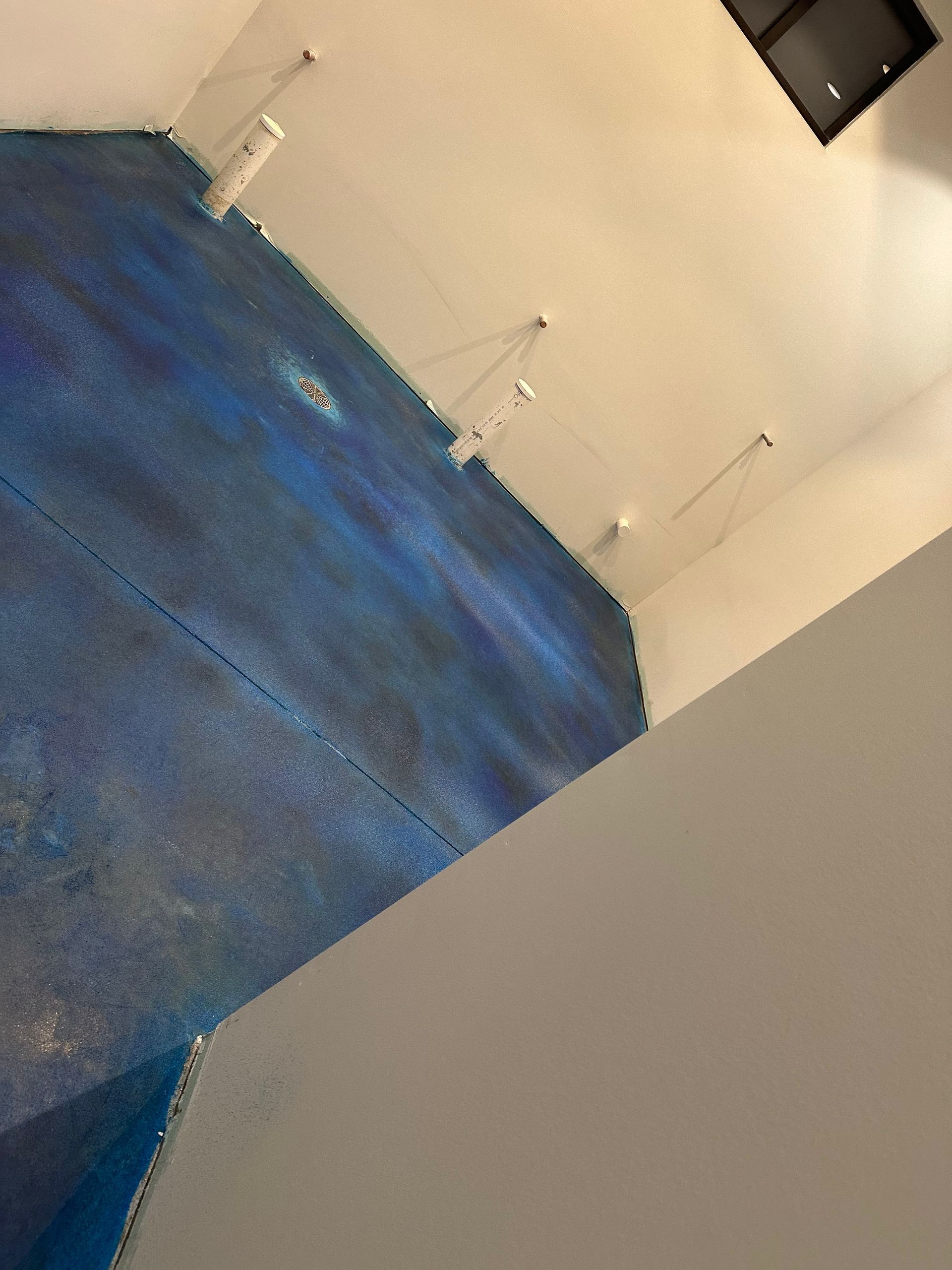 Tilted view of a room with a blue carpet and white walls, plus a wall-mounted TV and small fixtures above.