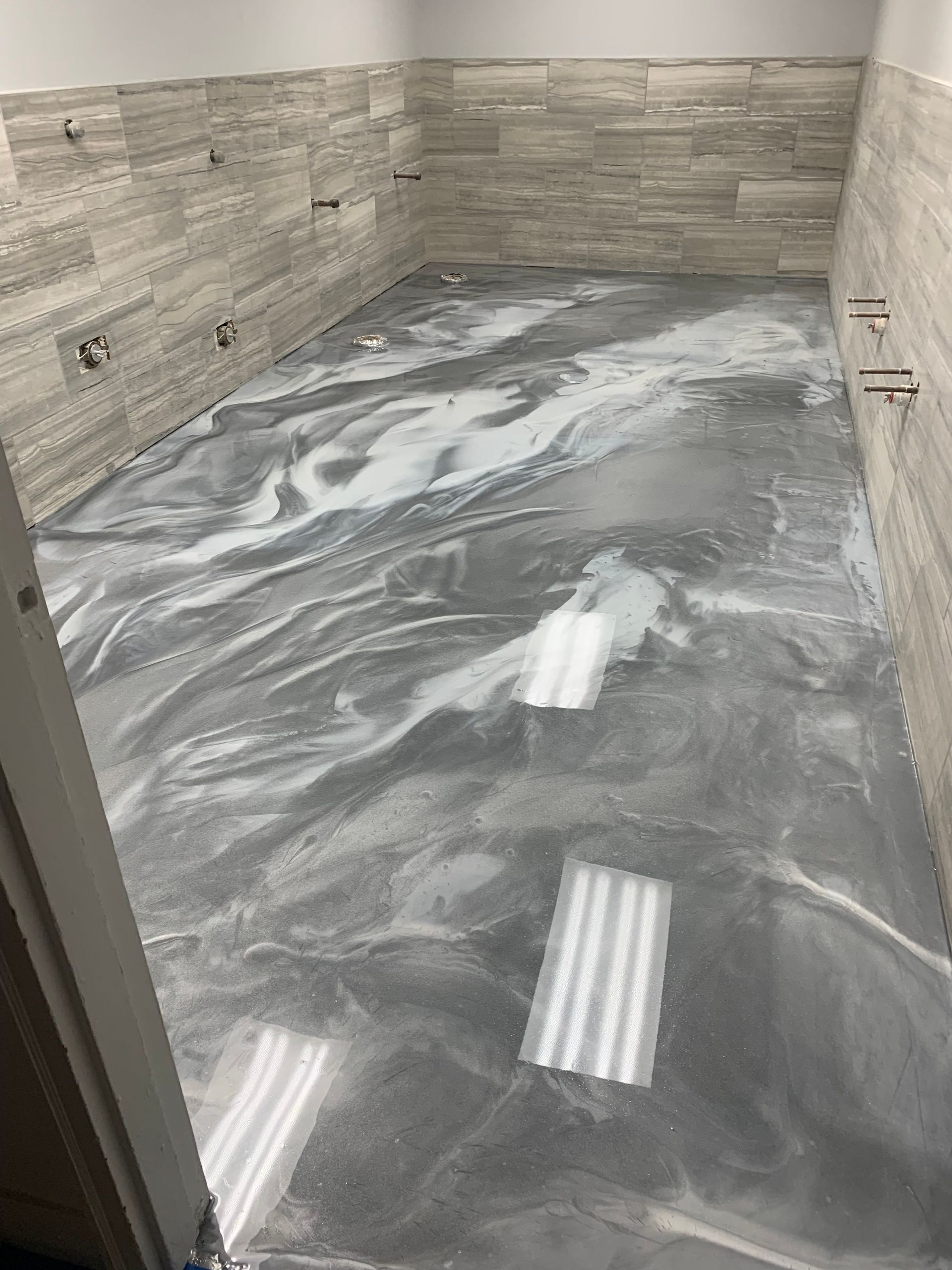 Empty tiled room with a marbled gray floor and stone-patterned walls, lit by ceiling reflections