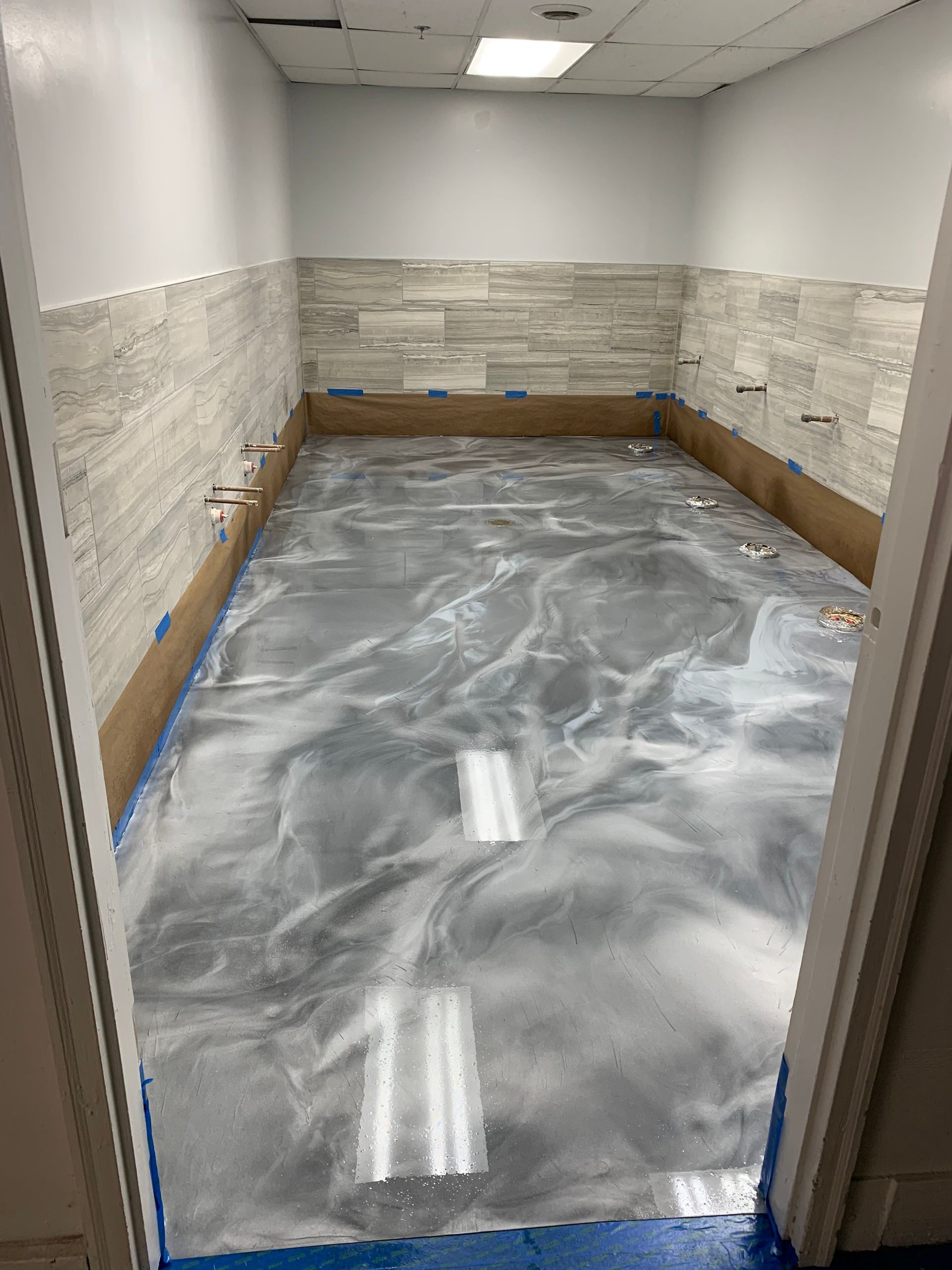 Empty tiled room with a freshly poured gray floor and white ceiling lights, viewed through a doorway