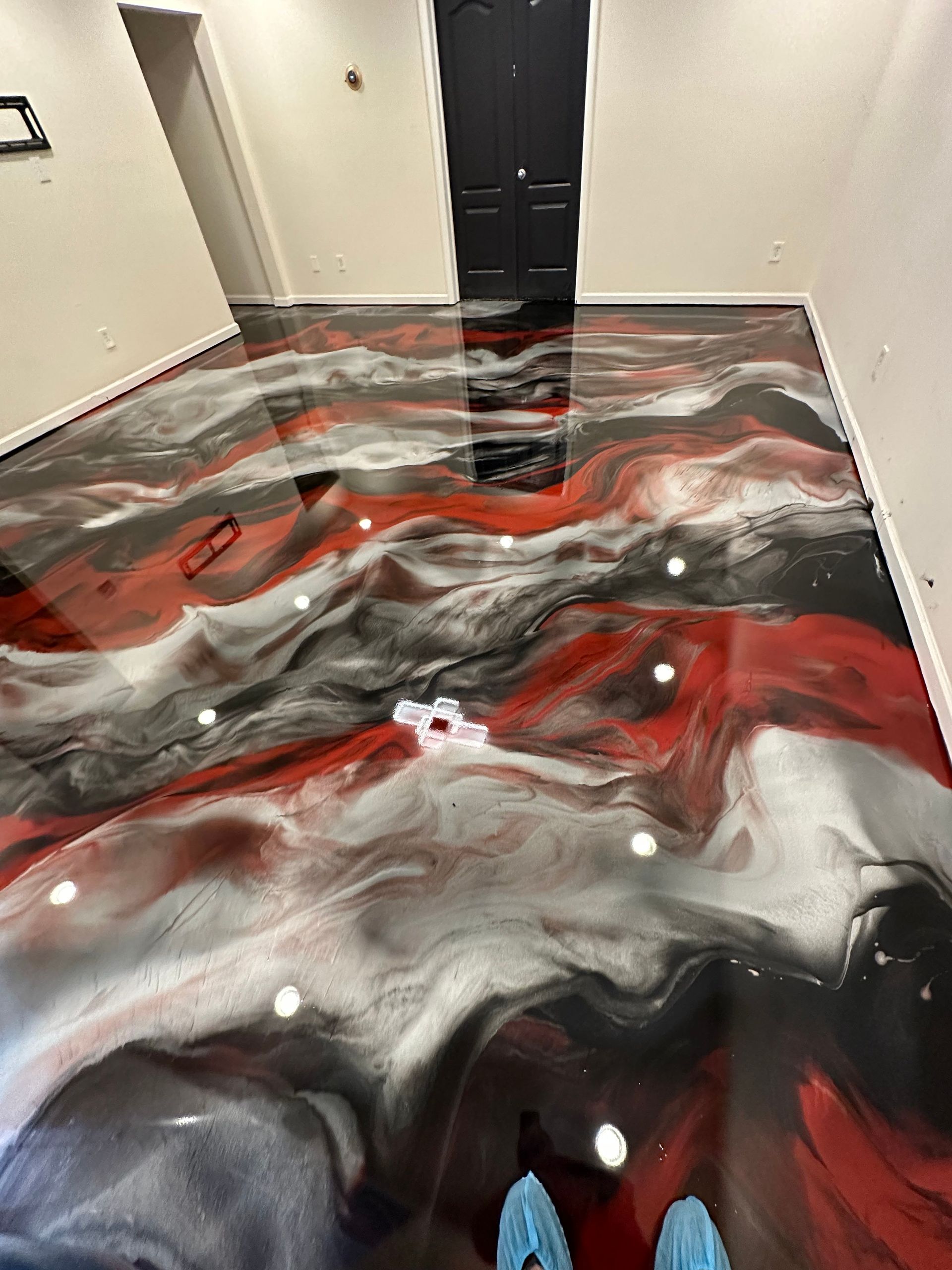Red, black, and white swirled epoxy floor in a hallway with black doors and white walls.