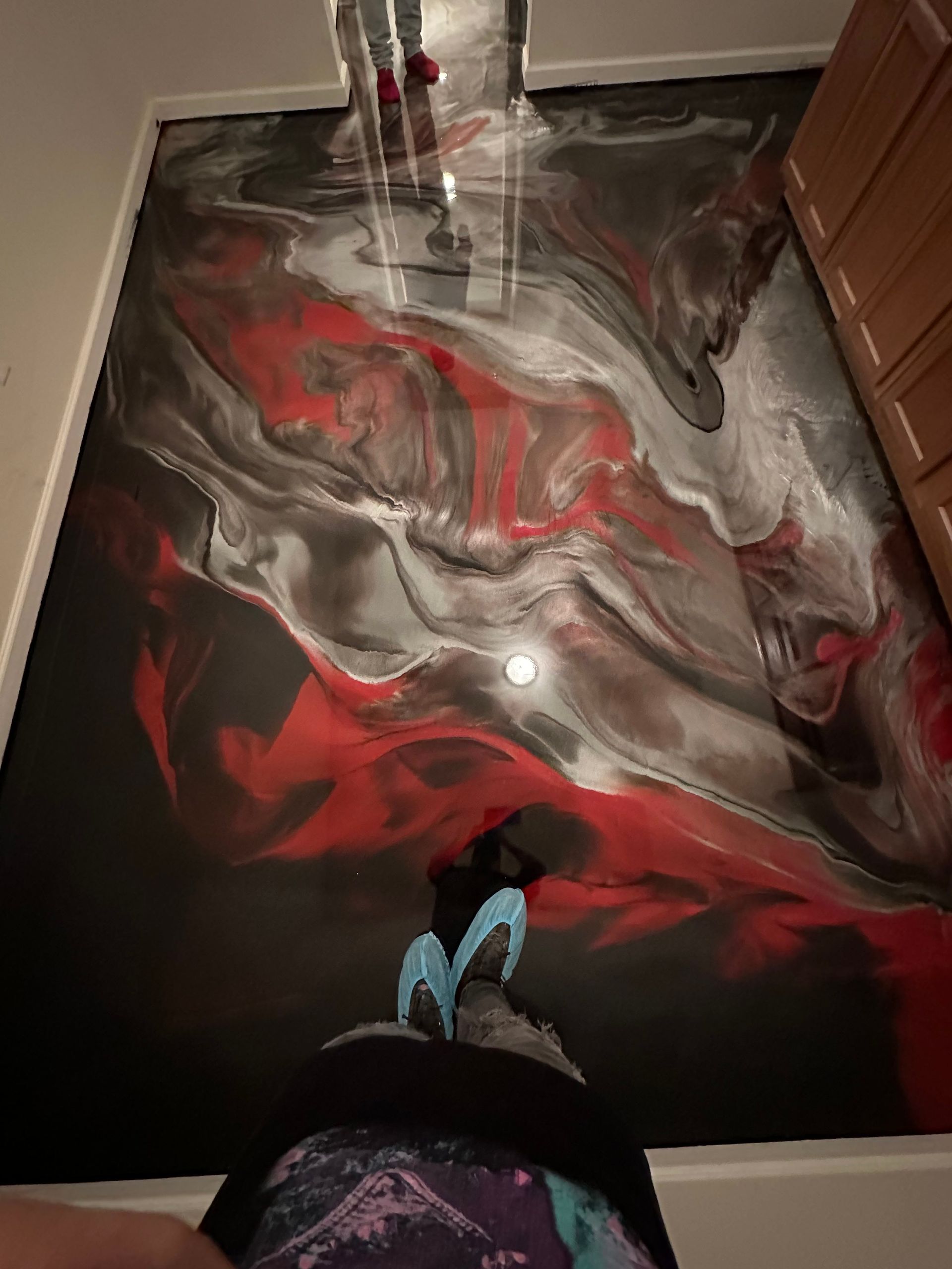 Abstract red, gray, and black fluid painting on a wall, viewed from below.