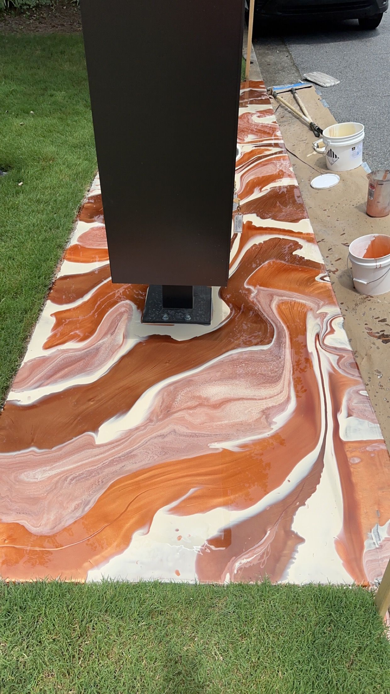 Orange and white marbled resin slab around a black metal post on grass outdoors