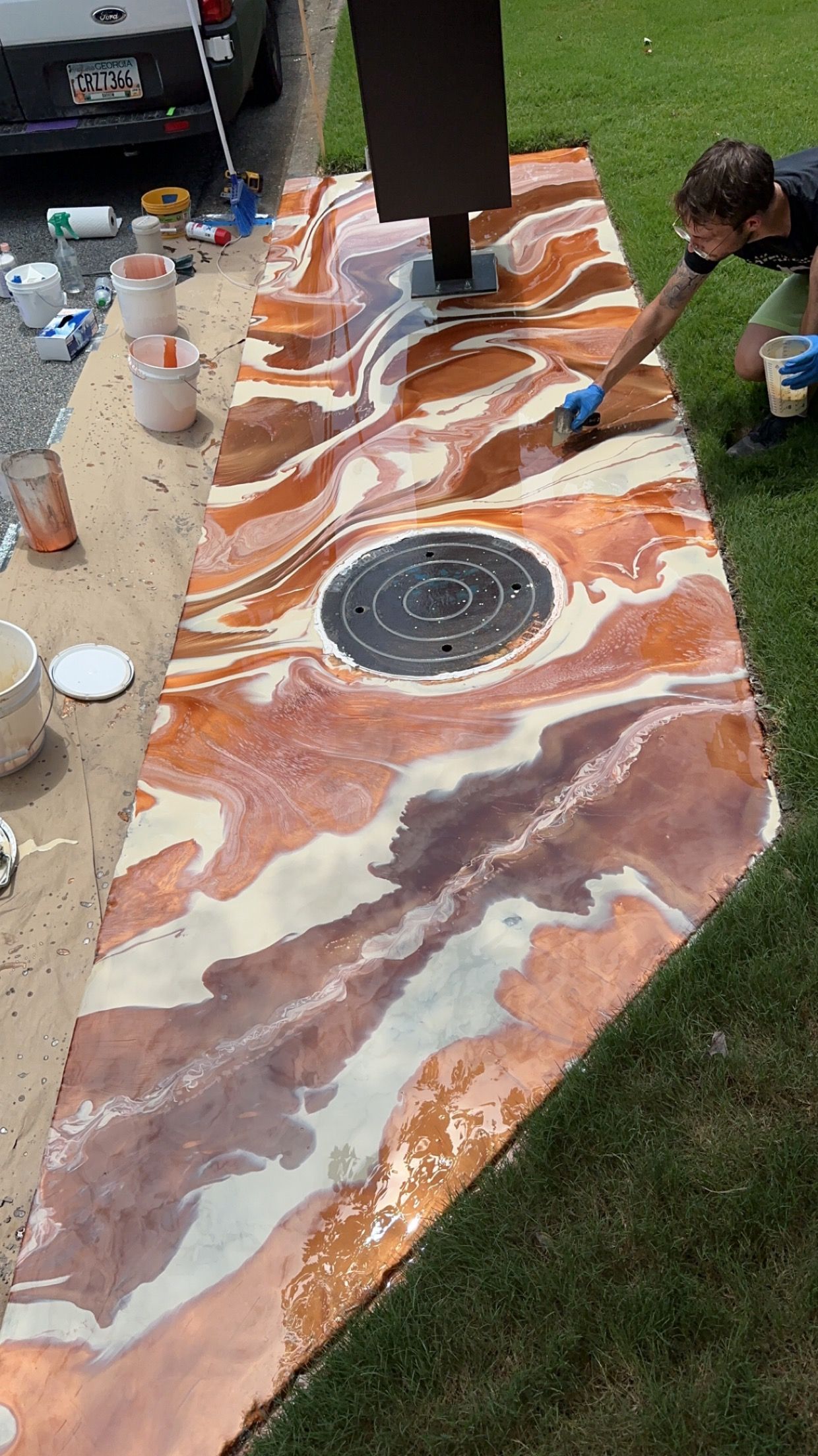 People applying marbled epoxy on a long outdoor table with a round sink in the center.
