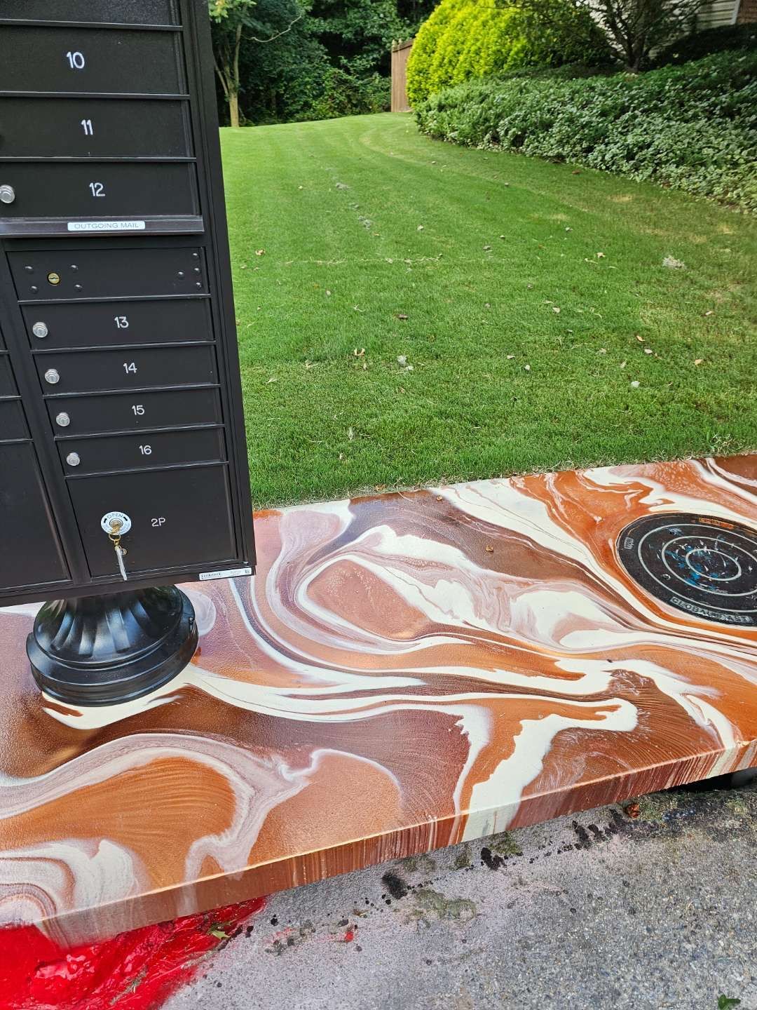 Abstract painted concrete step beside a lawn, with a black mailbox post on the left