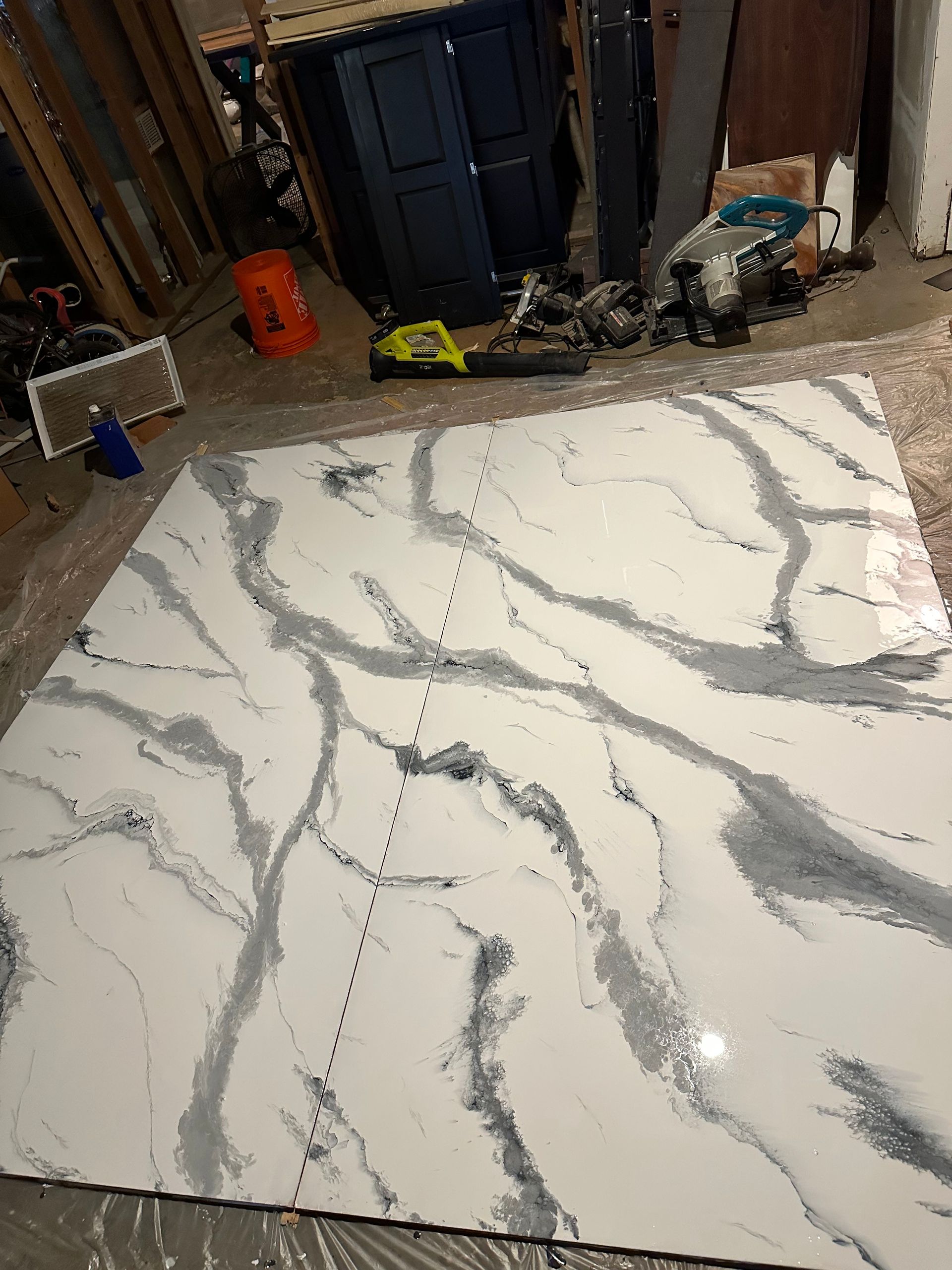 Large white marble-look tile slab with gray veining in a workshop or garage, surrounded by tools and cabinets.