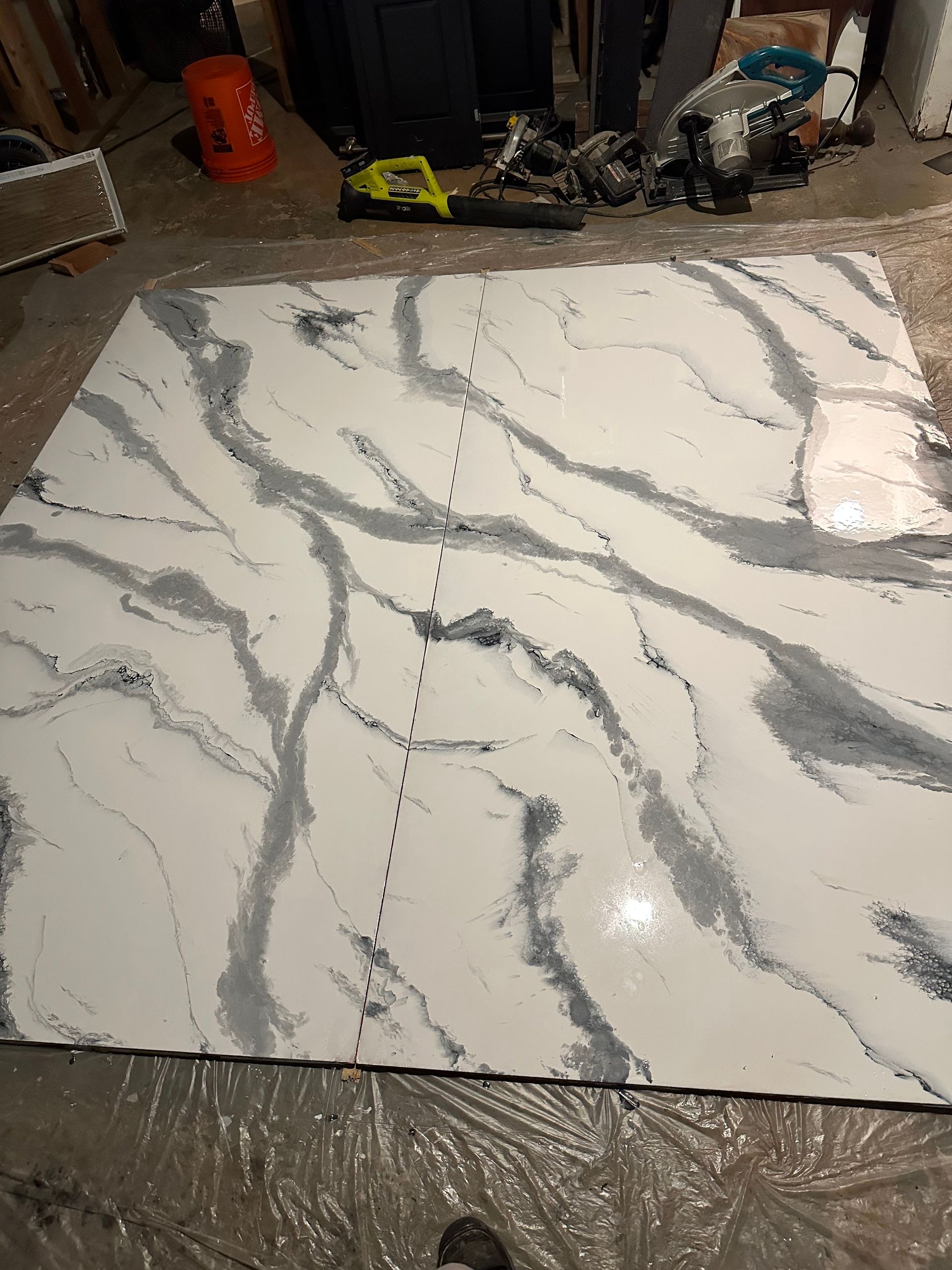 Large white marble-look tile with gray veining laid on a wet floor in a workshop area.