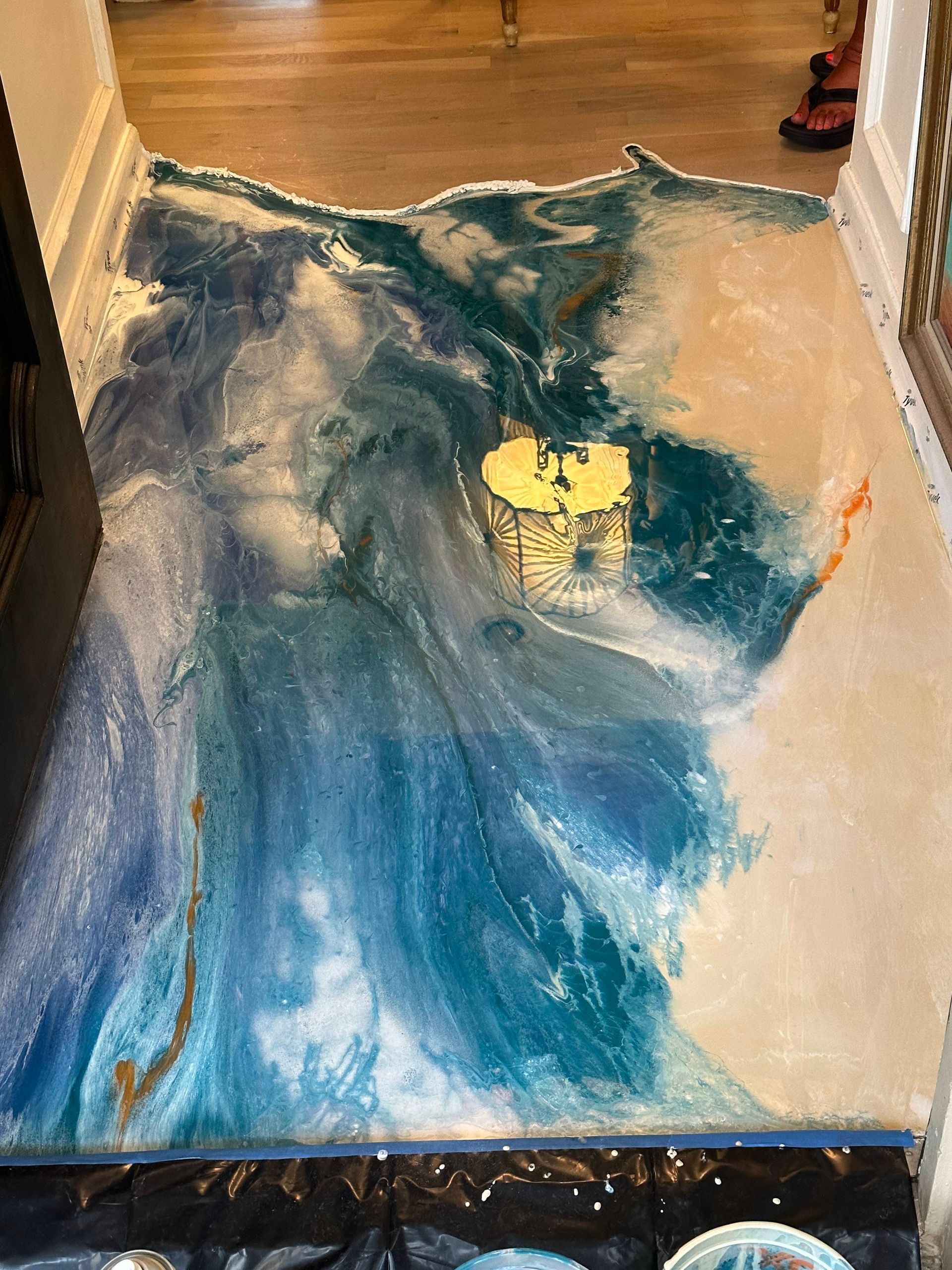 Blue and white wave-like resin art on a floor between walls, with a bright yellow center and black edging