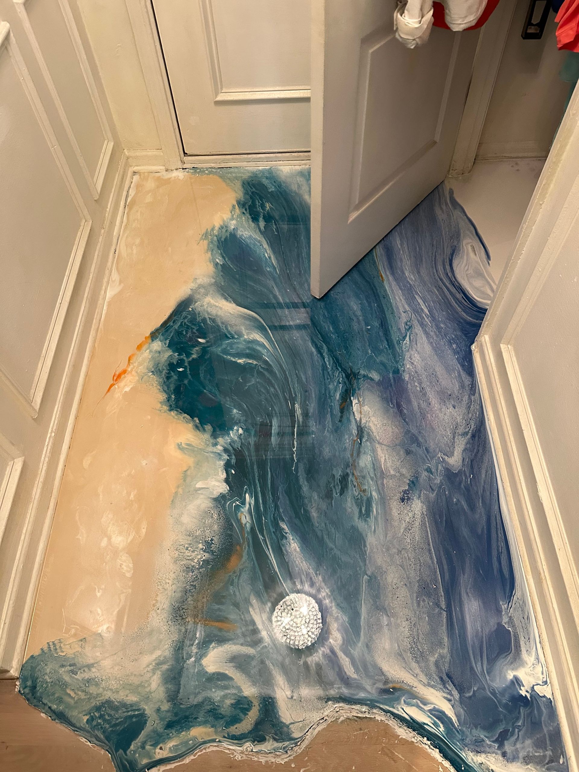 Blue and beige liquid spill flooding a bathroom floor near an open door and drain