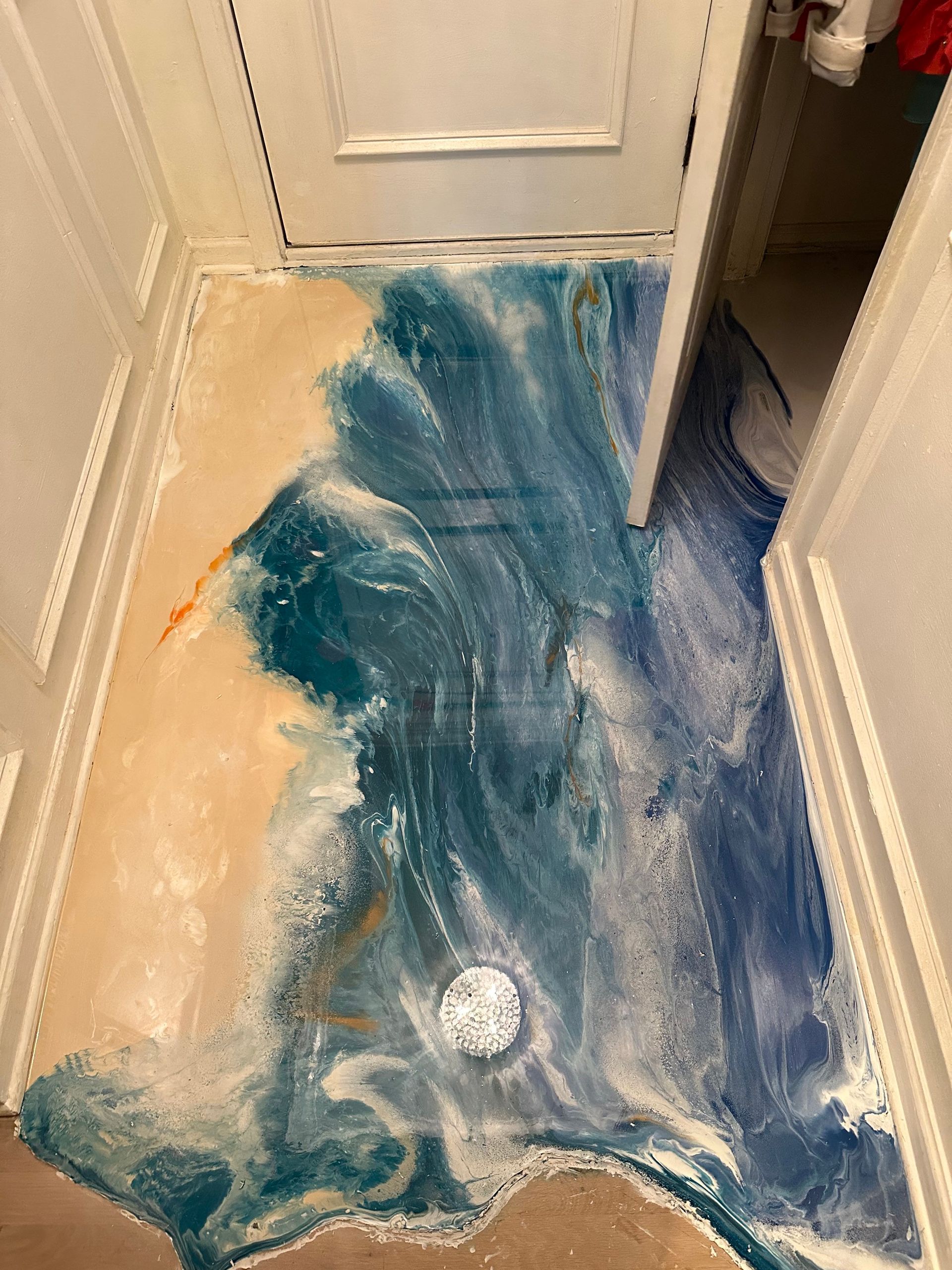 Blue liquid spilled across a hallway floor near a door, with a drain cover visible.