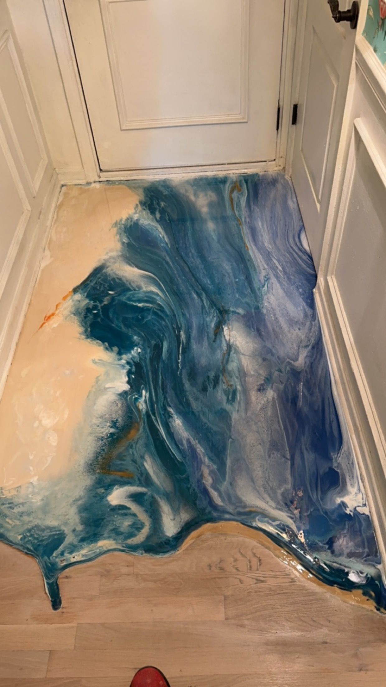 Blue-and-white resin spill spread across a hallway floor near a white door and cabinet.